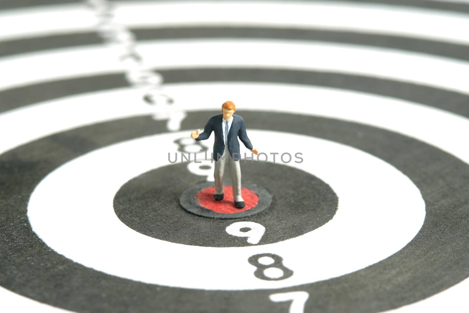 Miniature people toy figure photography. A shrugging businessman standing the center of dartboard. Isolated on white background. Image photo