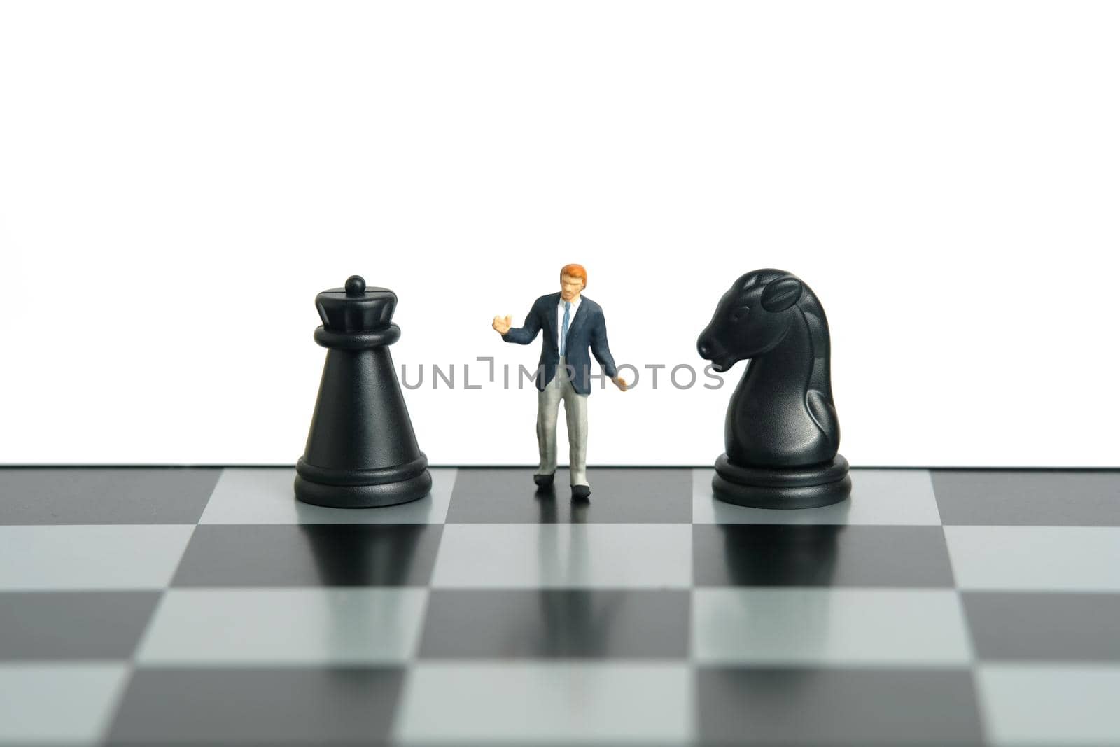 Miniature people toy figure photography. Attack or defense strategy decision concept. A shrugging businessman stand above chessboard with black horse and castle knight pawn. Isolated on white background. Image photo