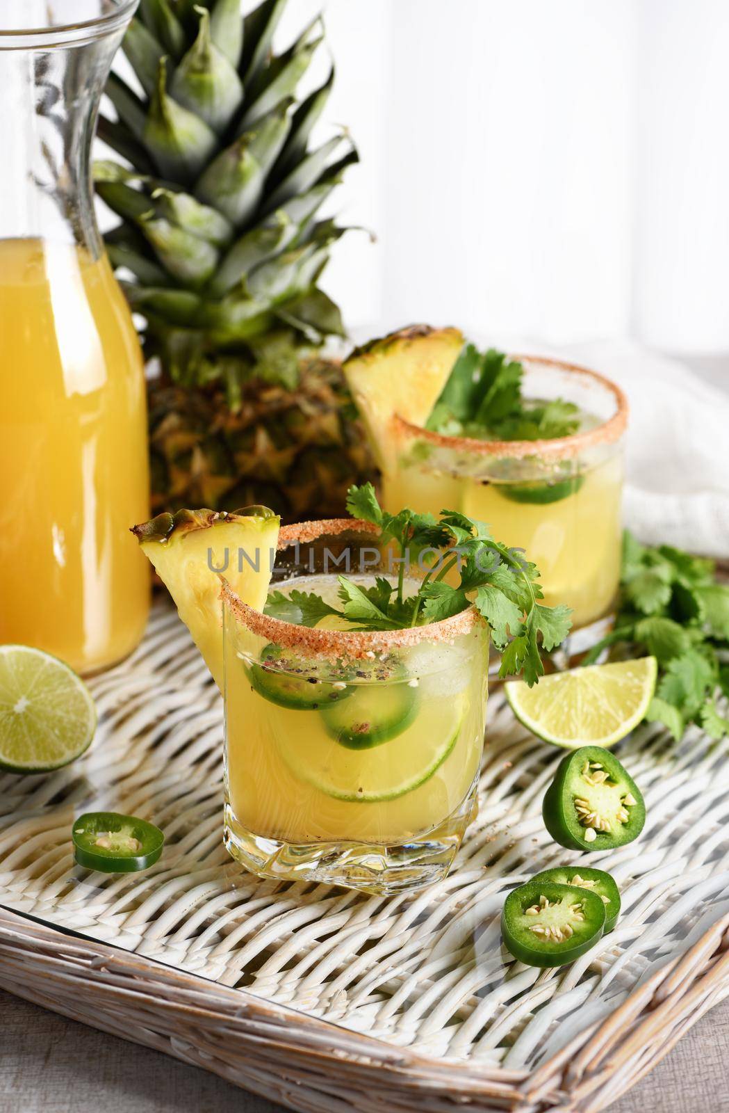 Spicy pineapple margarita with jalapeno slices, lime and cilantro sprigs