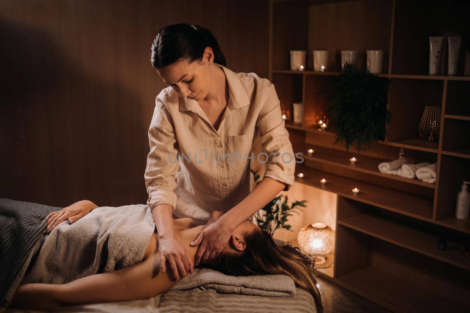 A masseuse gives a body massage to a woman in a spa center. A professional masseur massages the shoulder of a girl lying in a spa center.