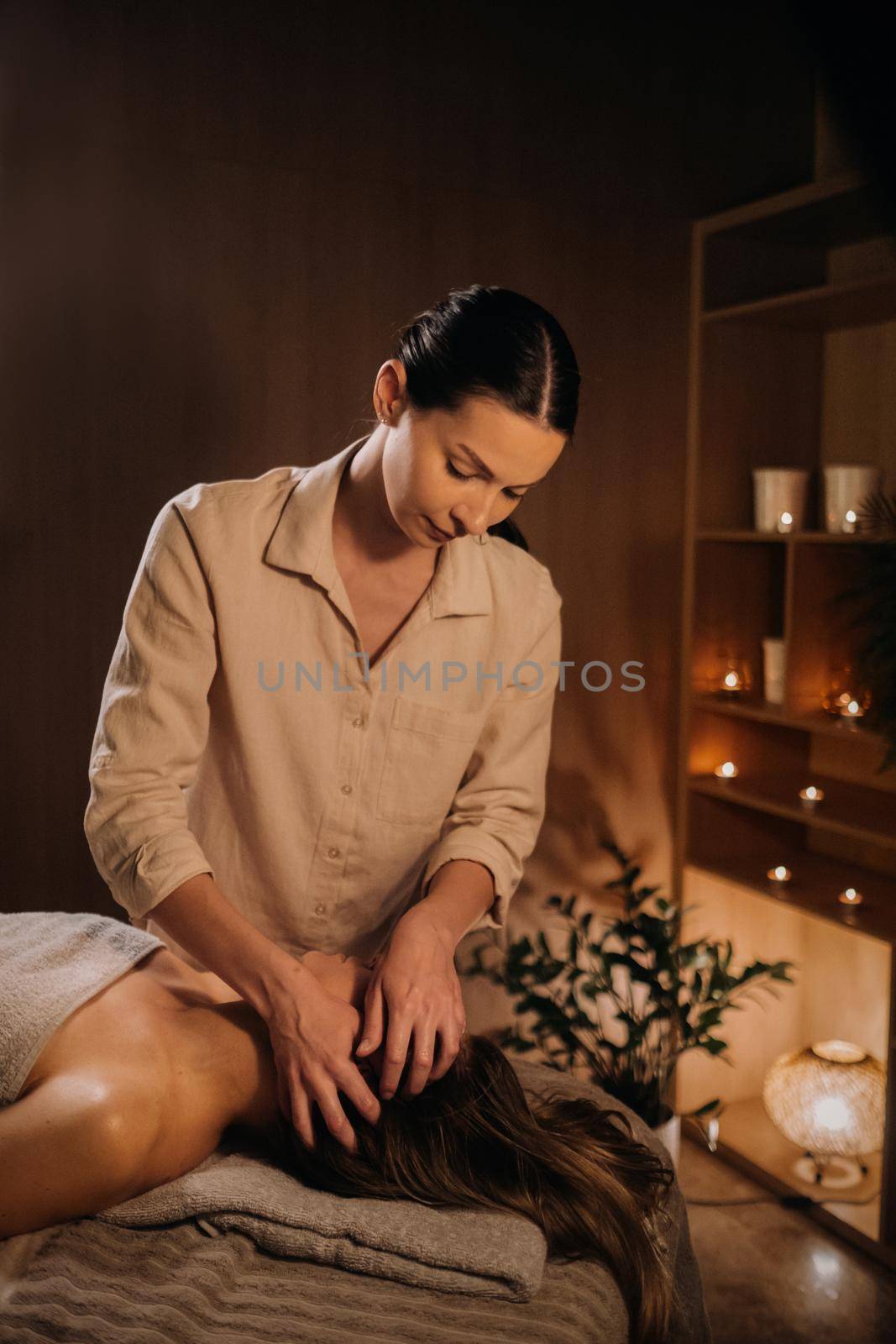 A masseuse gives a head massage to a woman at the spa. A professional masseur massages the head of a girl lying in a spa center by Lobachad