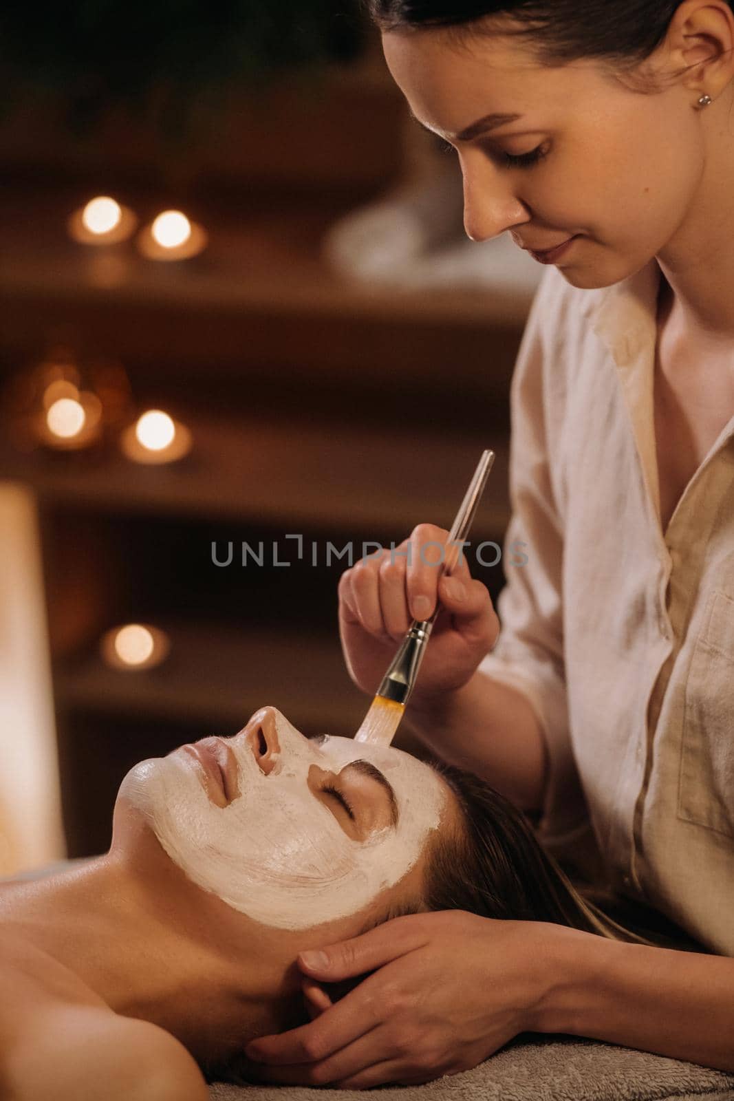 A cosmetologist makes a mask for a woman's face to rejuvenate the skin. Cosmetology by Lobachad