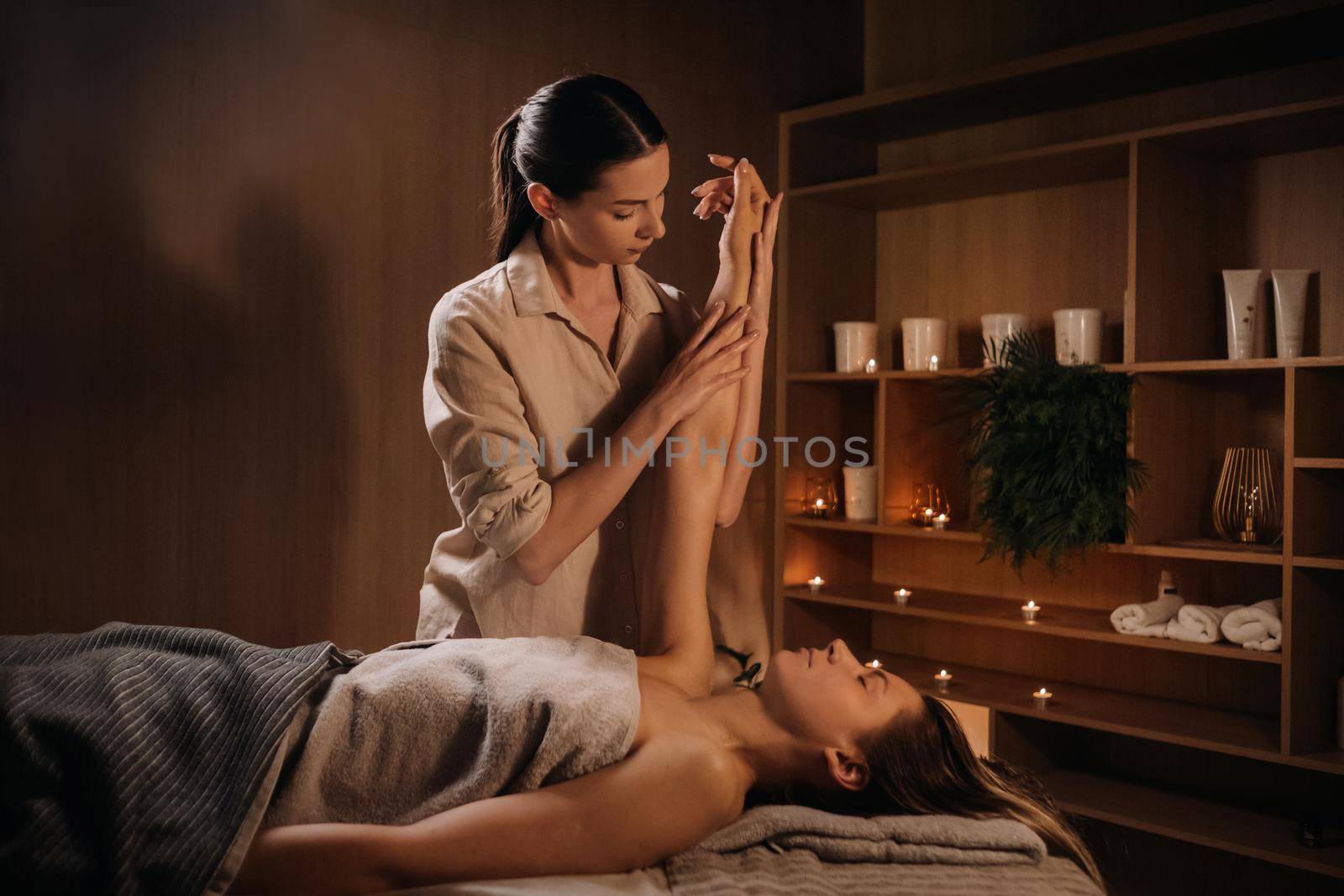 A masseuse gives a hand massage to a woman in a spa center. A professional masseur massages the hand of a girl lying in a spa center.