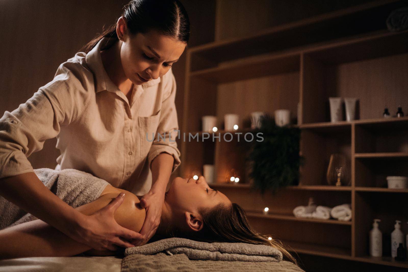 A masseuse gives a body massage to a woman in a spa center. A professional masseur massages the shoulder of a girl lying in a spa center.