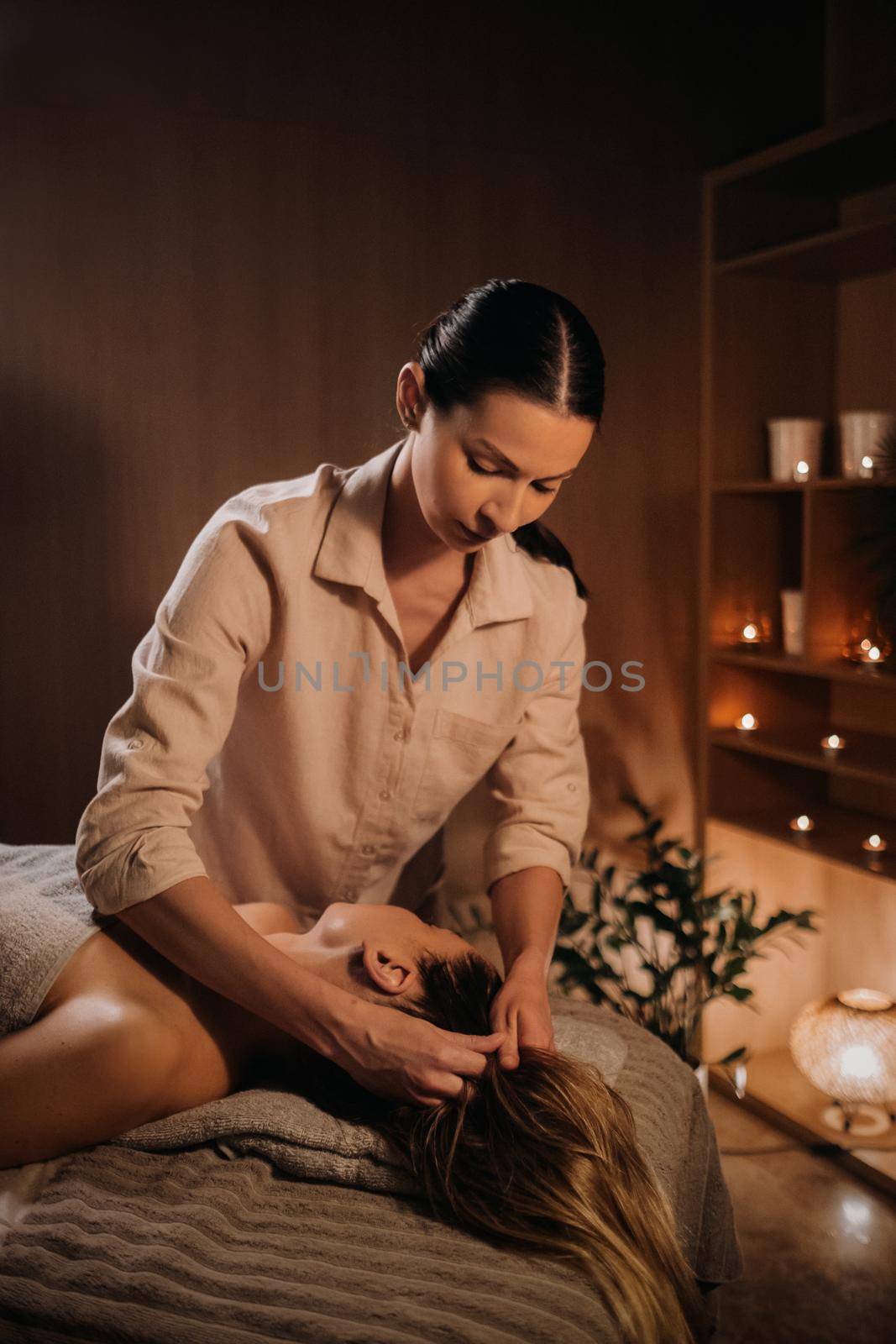 A masseuse gives a head massage to a woman at the spa. A professional masseur massages the head of a girl lying in a spa center.