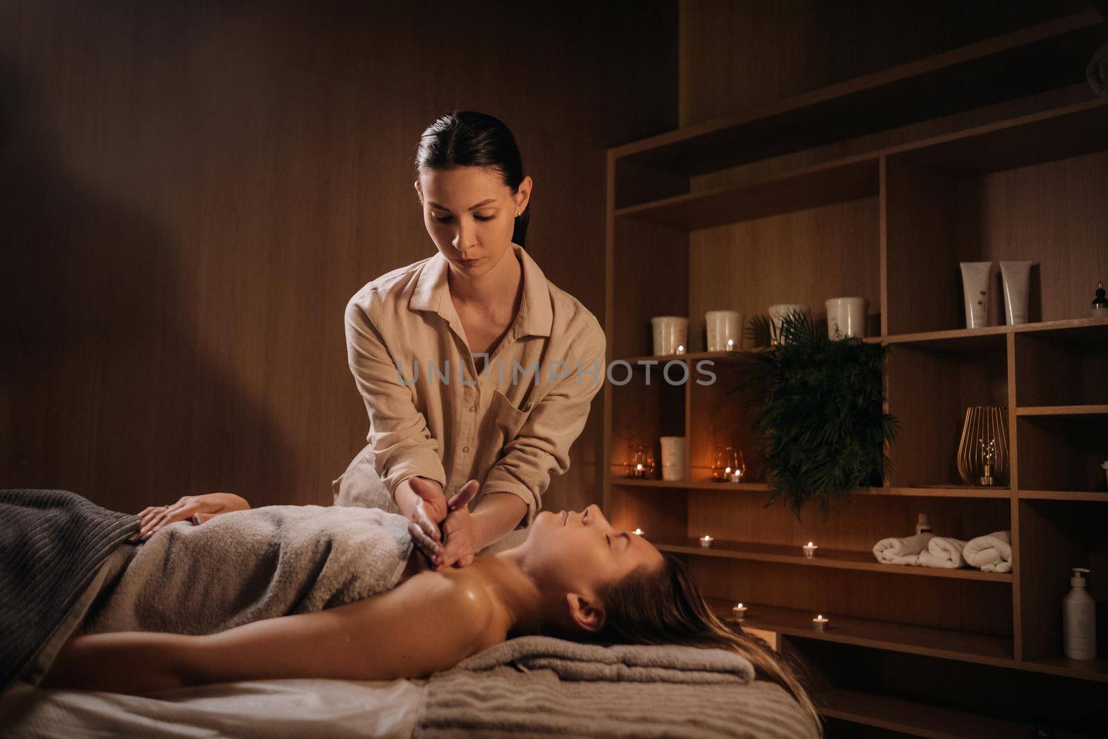 A masseuse gives a body massage to a woman in a spa center. A professional masseur massages the shoulder of a girl lying in a spa center.