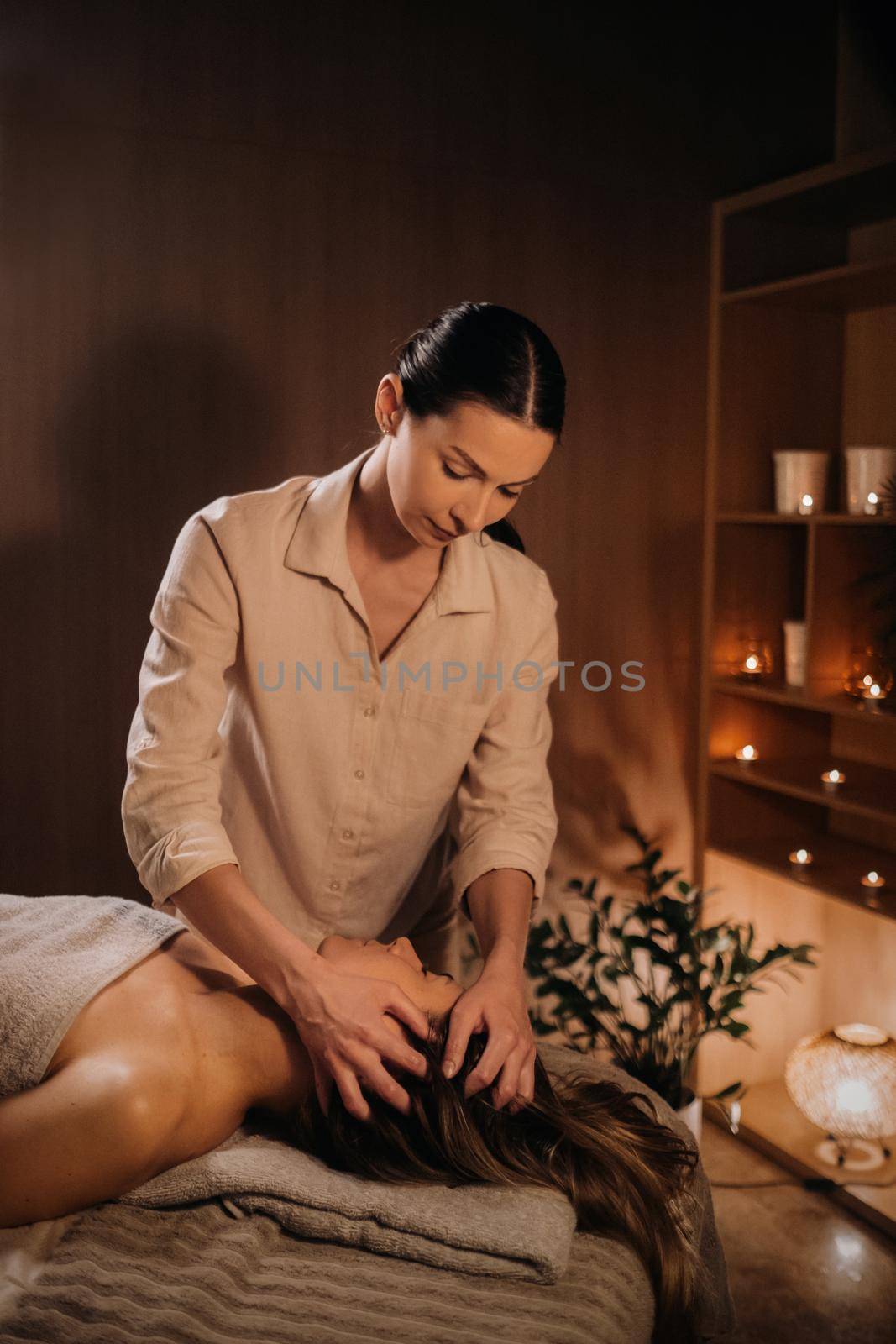 A masseuse gives a head massage to a woman at the spa. A professional masseur massages the head of a girl lying in a spa center by Lobachad