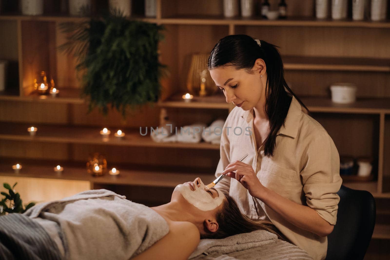 A cosmetologist makes a mask for a woman's face to rejuvenate the skin. Cosmetology.