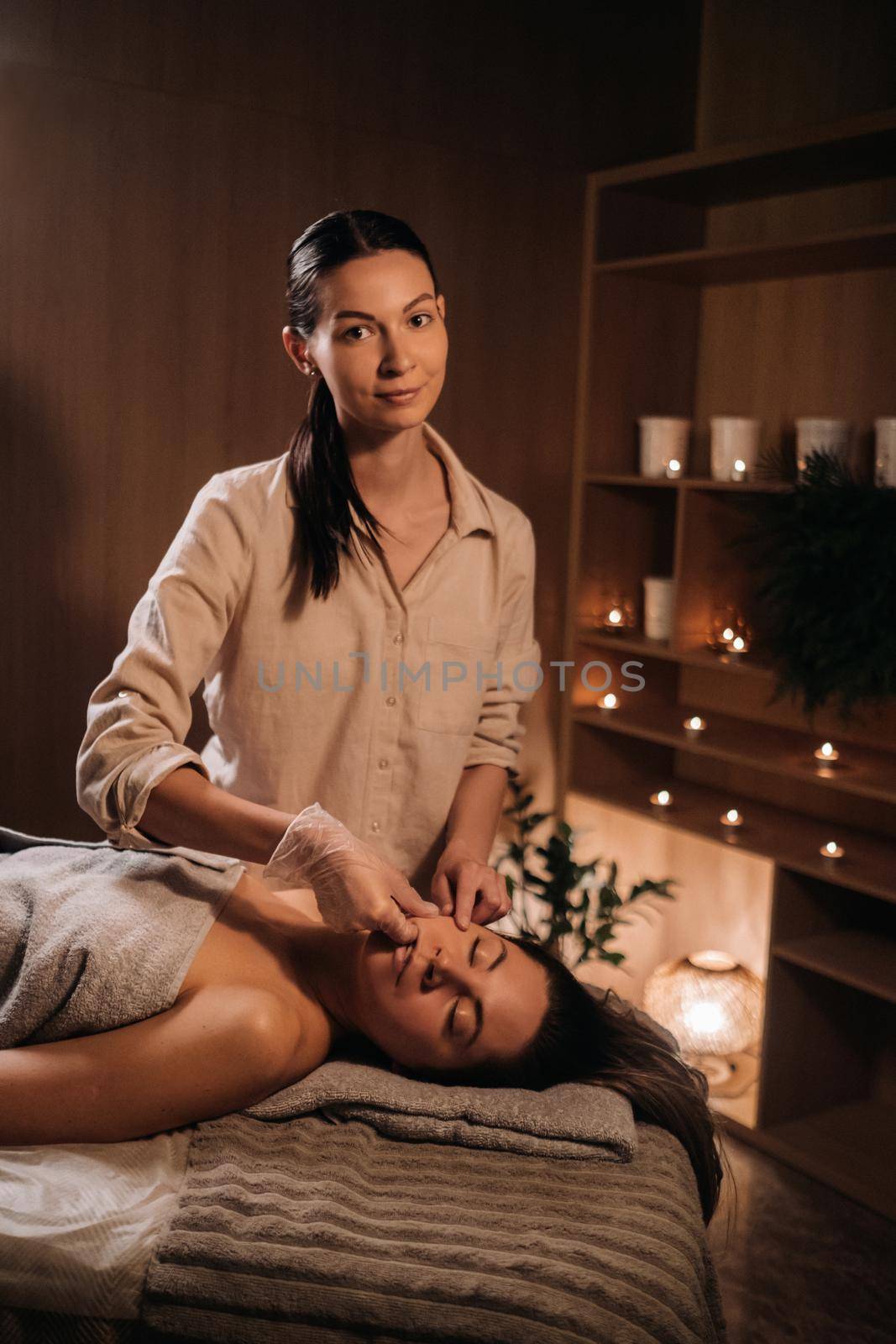 A cosmetologist girl does a facial and neck massage to a girl in the office for skin elasticity.