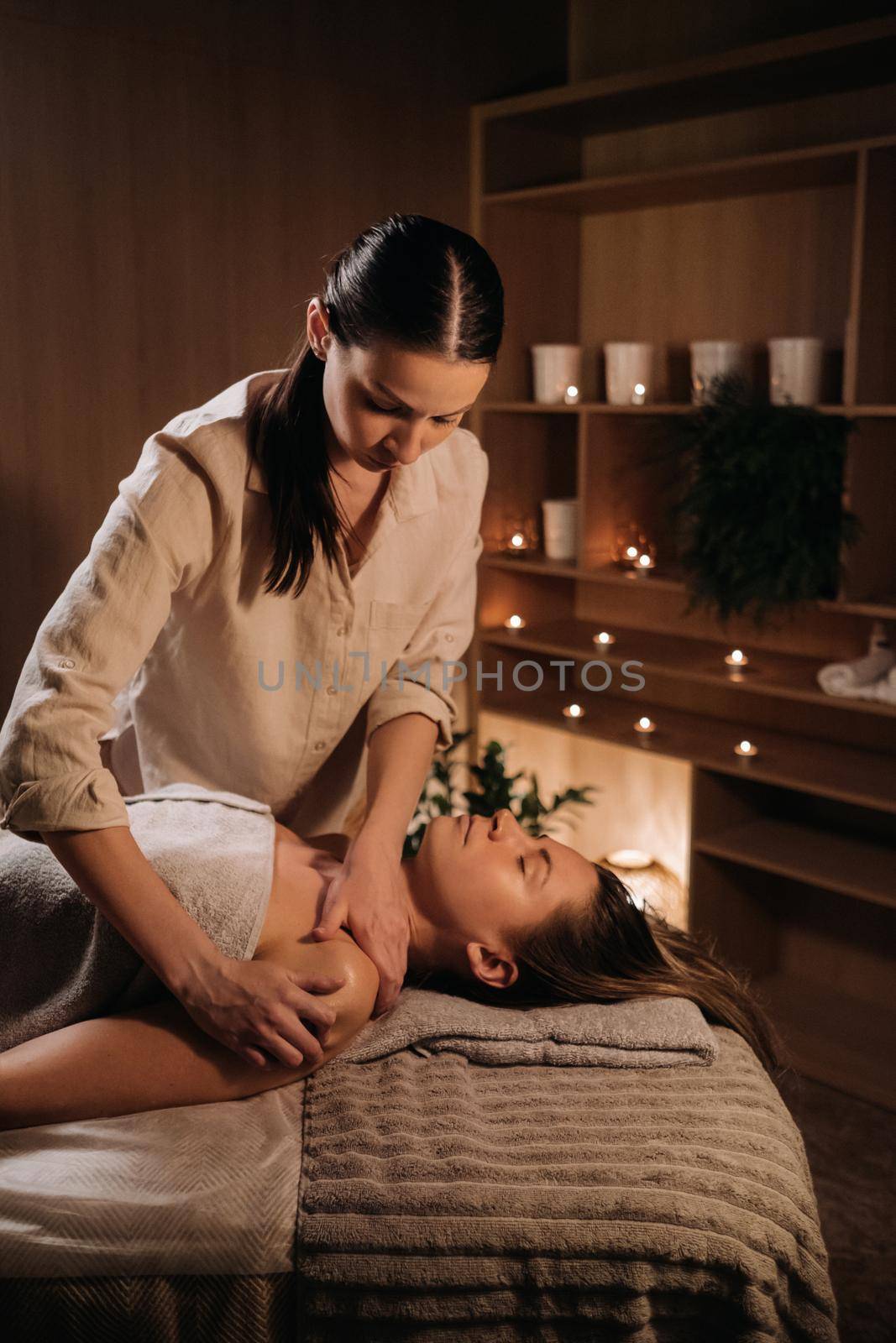 A masseuse gives a body massage to a woman in a spa center. A professional masseur massages the shoulder of a girl lying in a spa center.