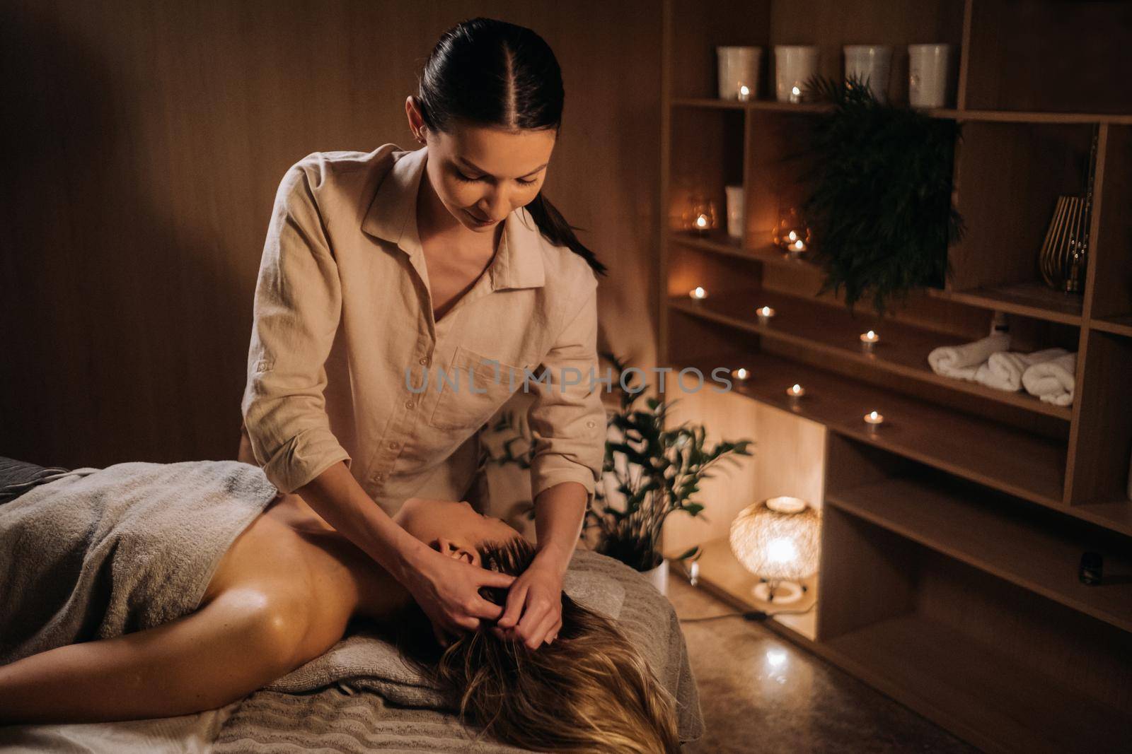 A masseuse gives a head massage to a woman at the spa. A professional masseur massages the head of a girl lying in a spa center.