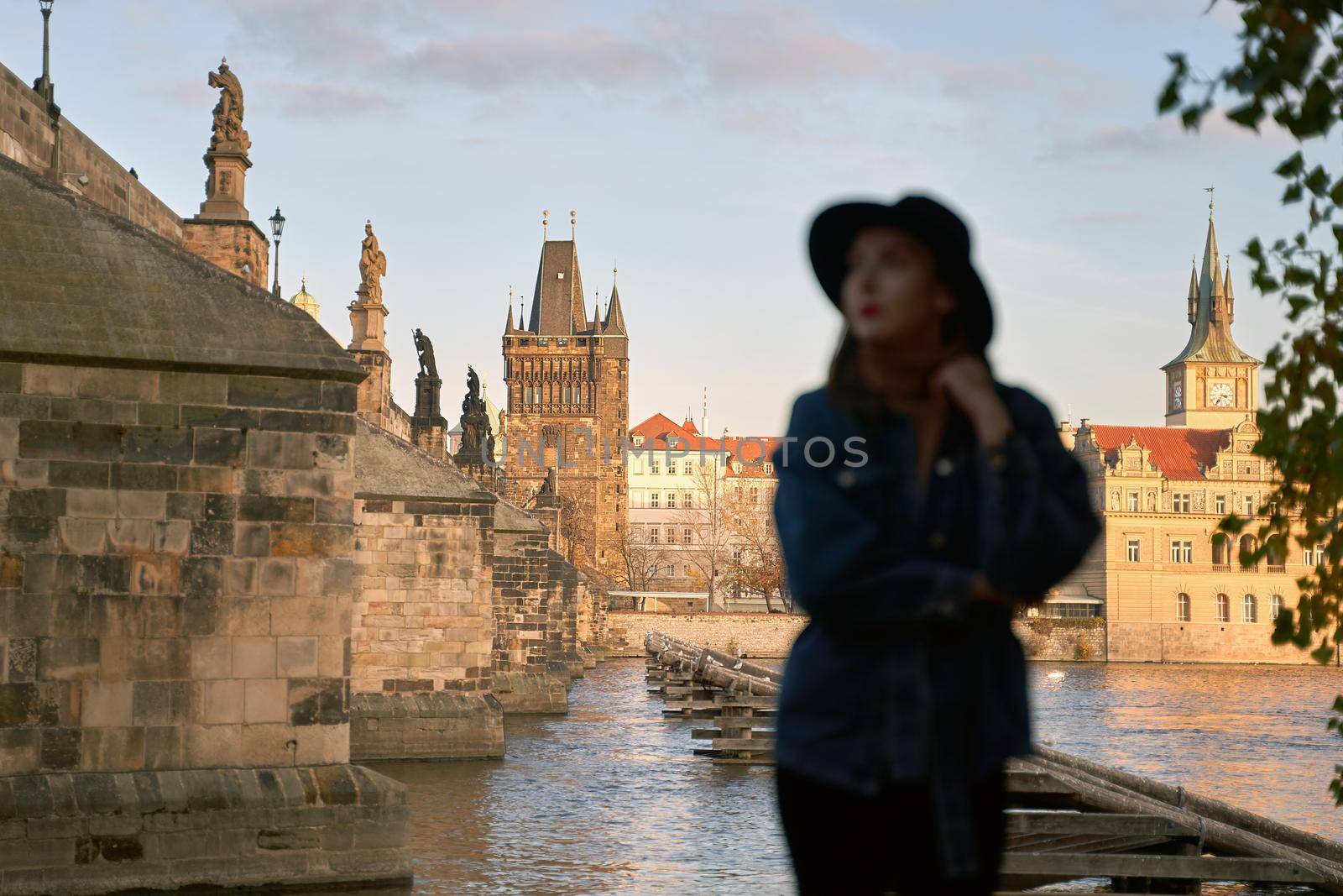 Prague Silhouette. Stylish beautiful young woman wearing black hat with Charles Bridge on background. Elegant retro lady fine art portrait. Focus on background. by berezko