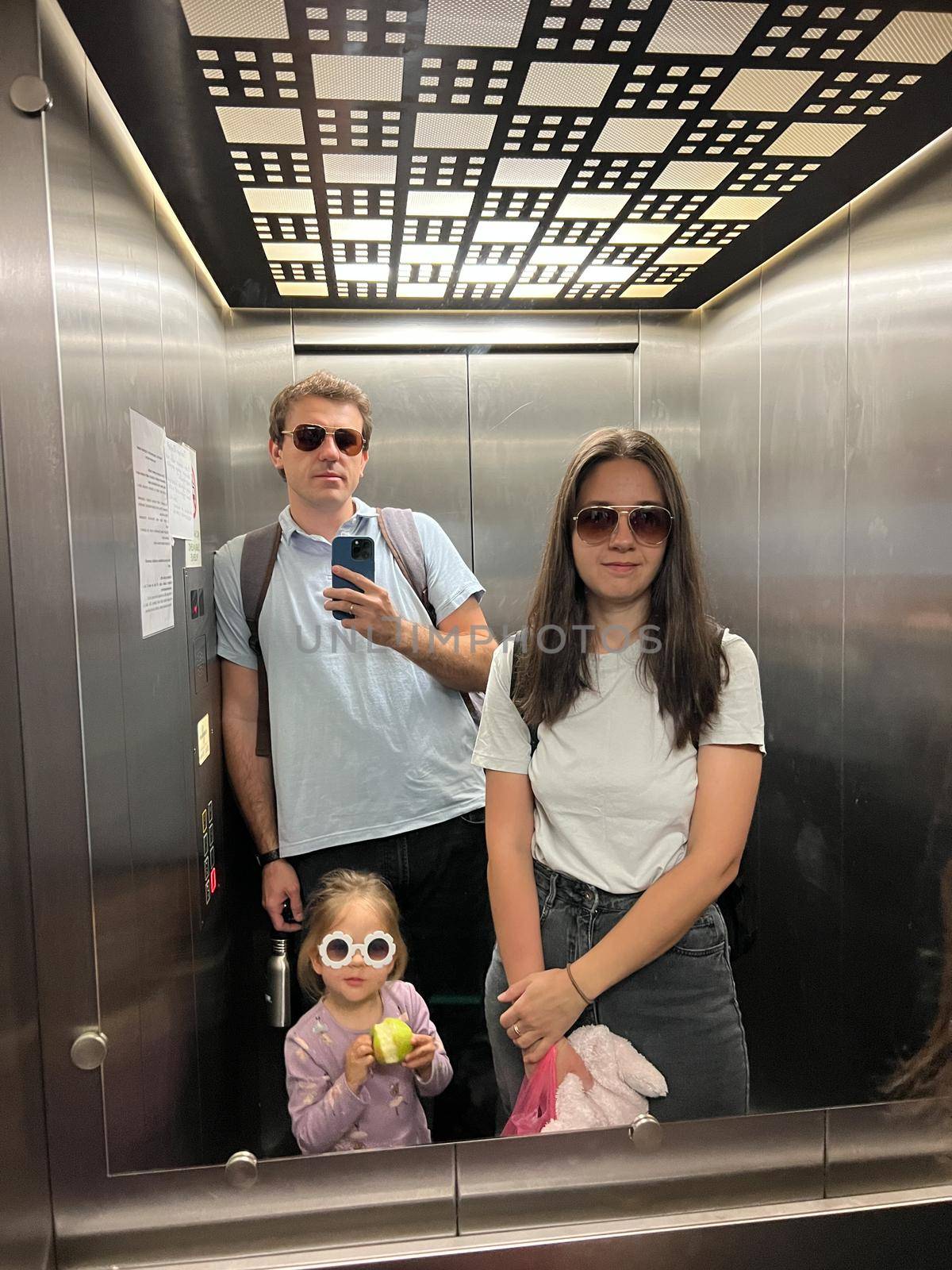 Mom, dad and a little girl are photographed in the elevator mirror on a smartphone. High quality photo