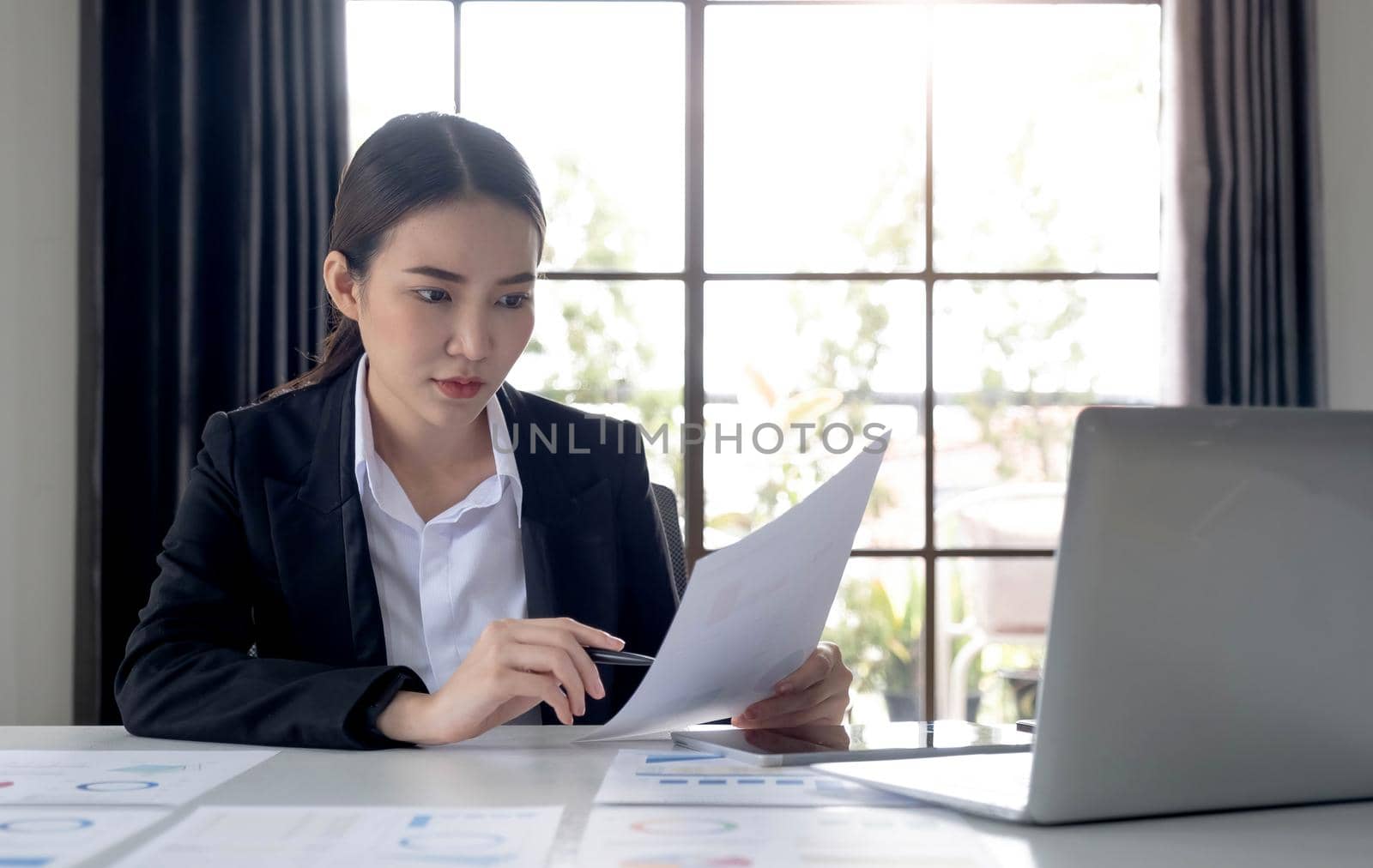 Portrait of an Asian woman working on a tablet computer in a modern office. Make an account analysis report. real estate investment information financial and tax system concepts by wichayada