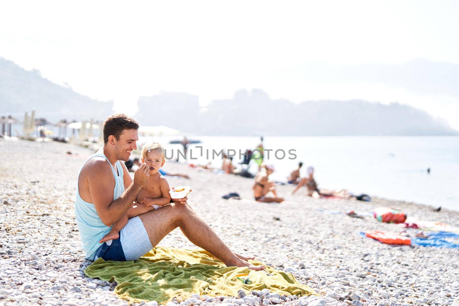 Dad feeding his little daughter with a spoon on the beach. High quality photo