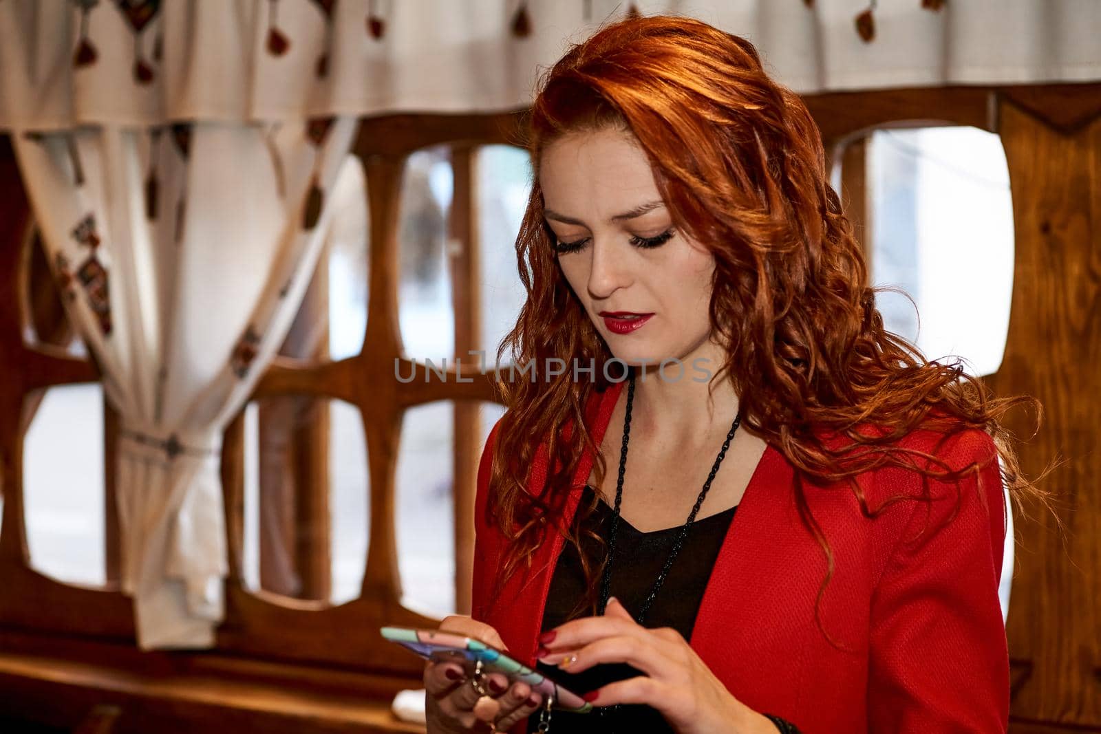 Serious pretty red-haired girl in a red jacket writes a message on the phone by jovani68