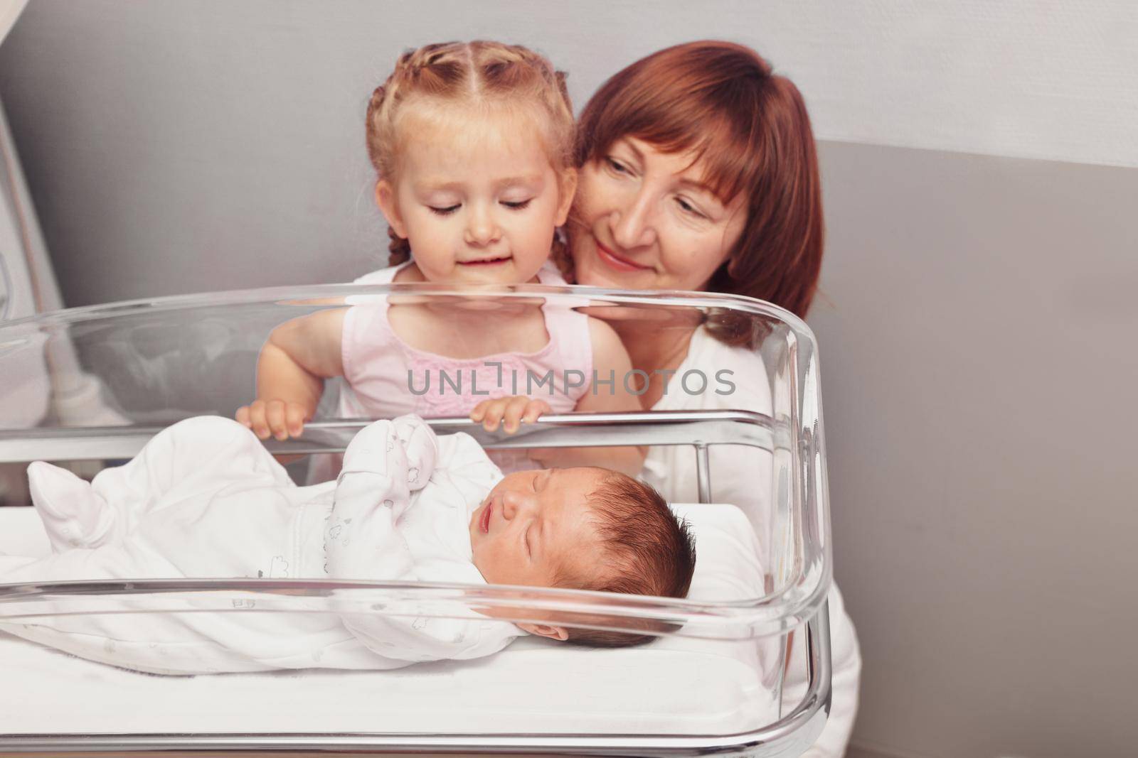 The sister and grandmother looks at a newborn baby in the hospital by Godi