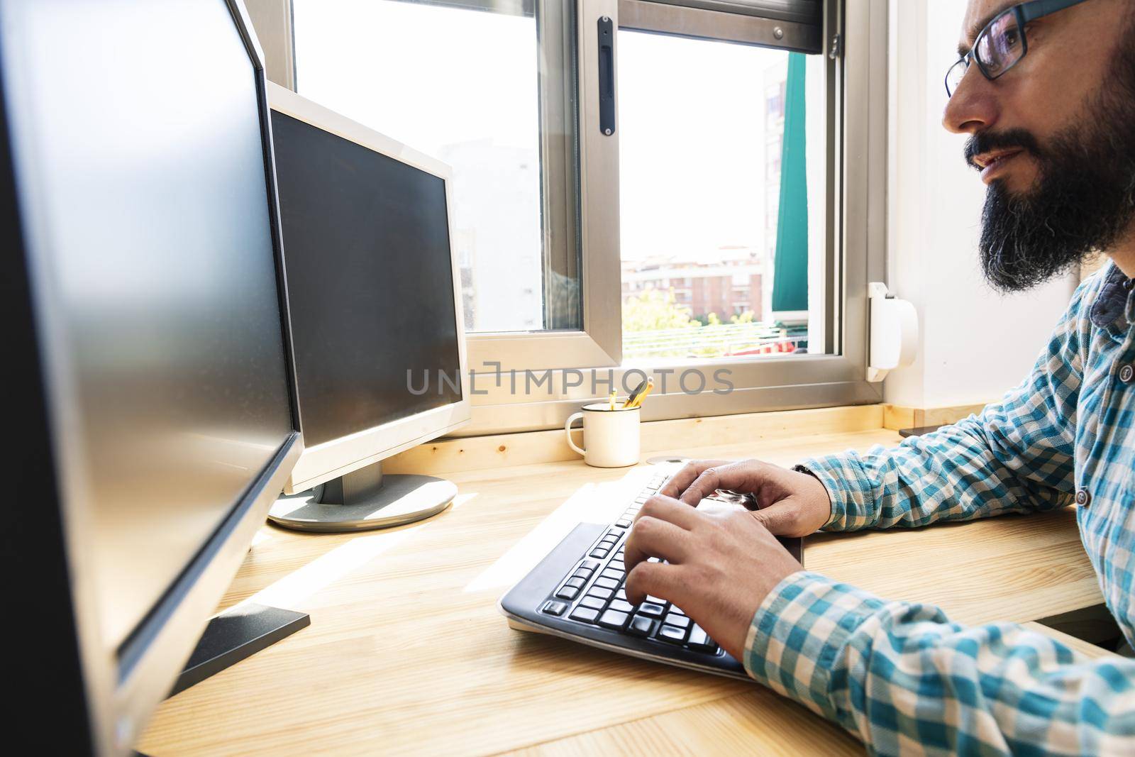 man typing on a keyboard in front of two computer screens, work from home concept