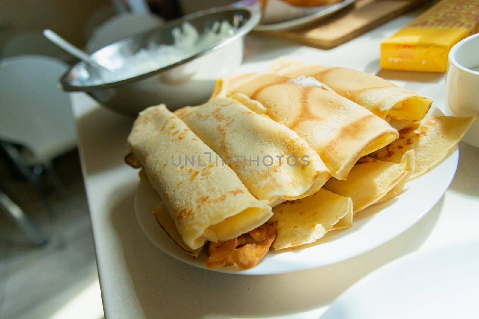 A stack of rolled pancakes on a plate in the sunlight, kitchen view