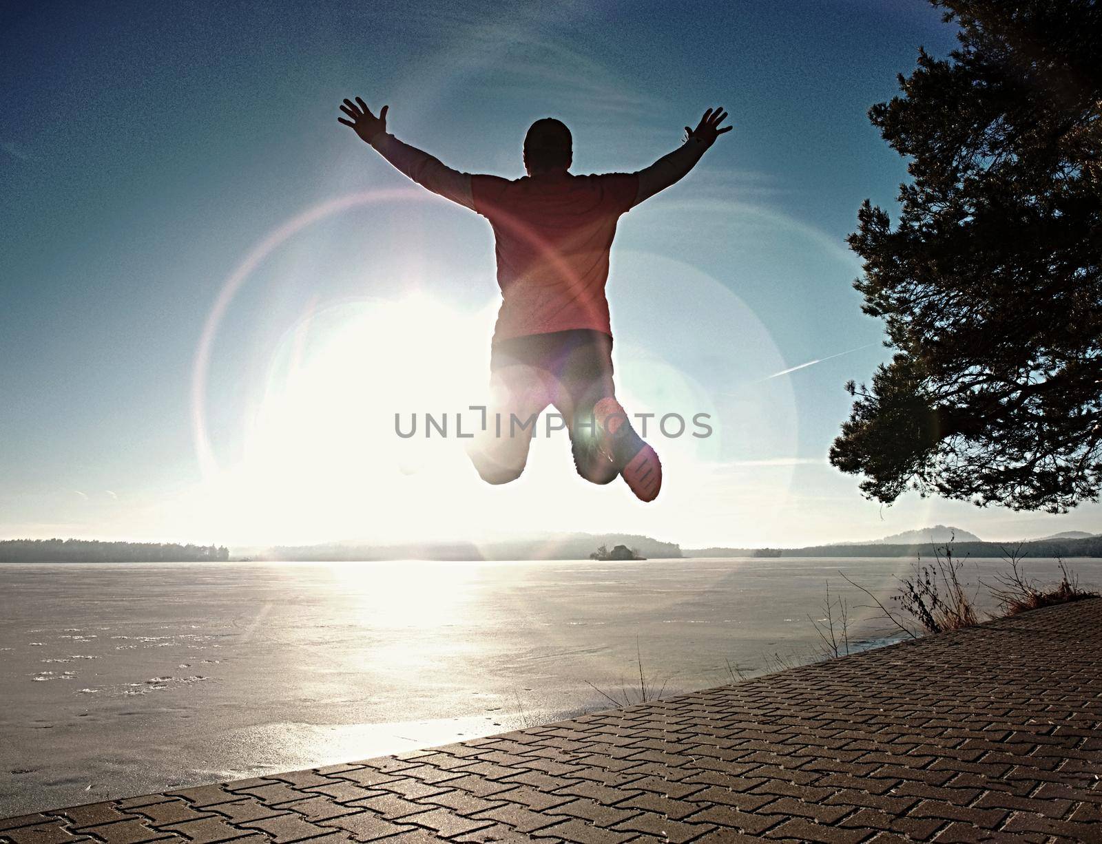 Crazy man jumping while joogging at morning spring lake bay. Sunny morning with clear blue sky above.