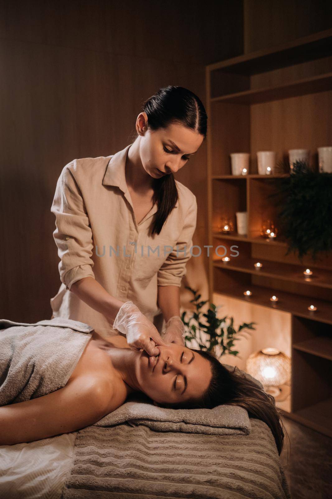 A cosmetologist girl does a facial and neck massage to a girl in the office for skin elasticity.