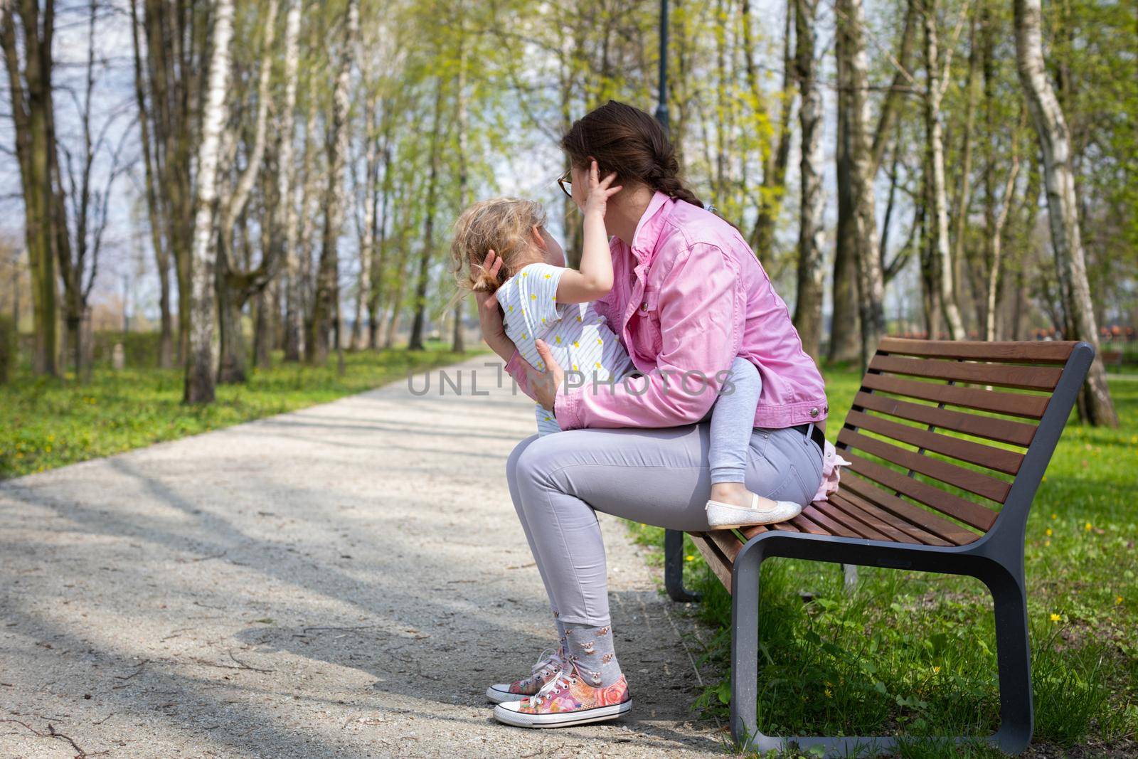 Exercise and play on a park bench. The caregiver swings the child up and down. A spring sunny day in a city park.