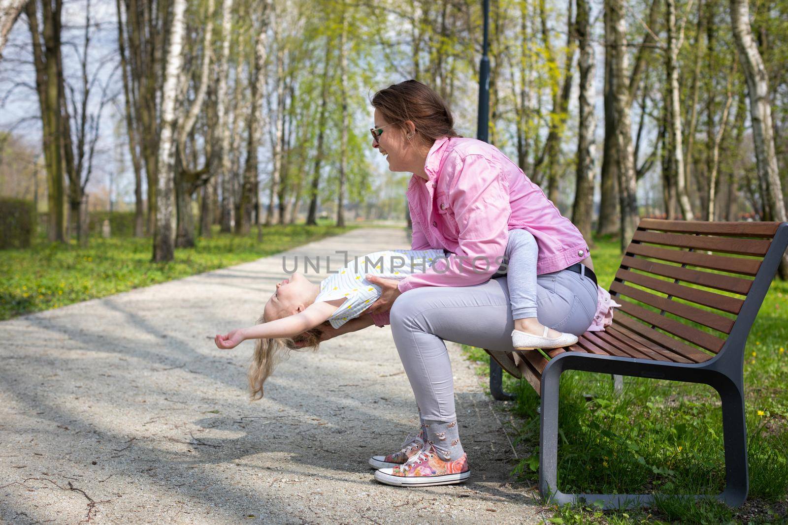 Outdoor gymnastics, mother and daughter, on a bench in the city park. Motor play with exercise of abdominal muscles in the child.