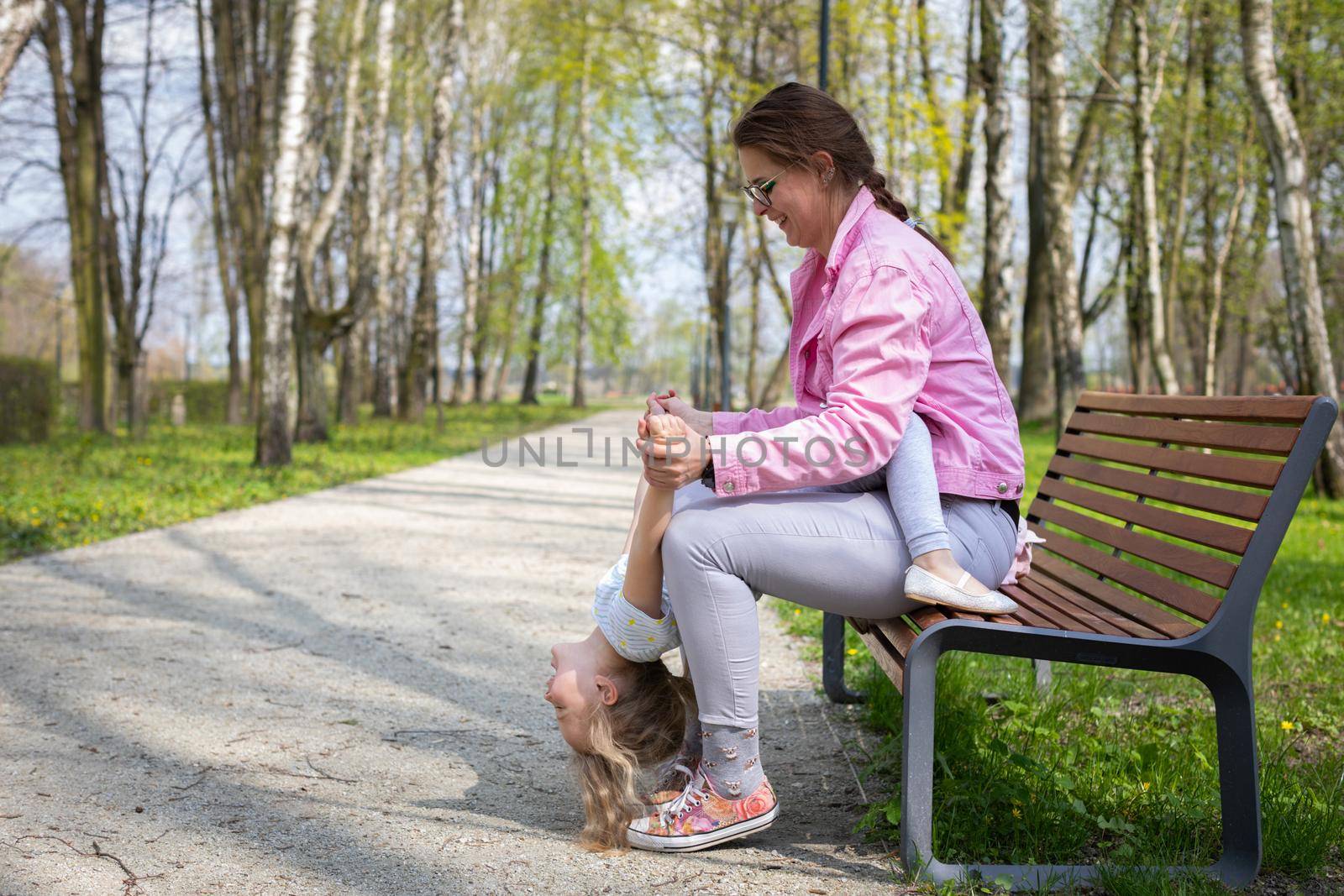 Mom and child do mini gymnastics on a bench in a city park. A movement game with abdominal muscle exercises in the child.