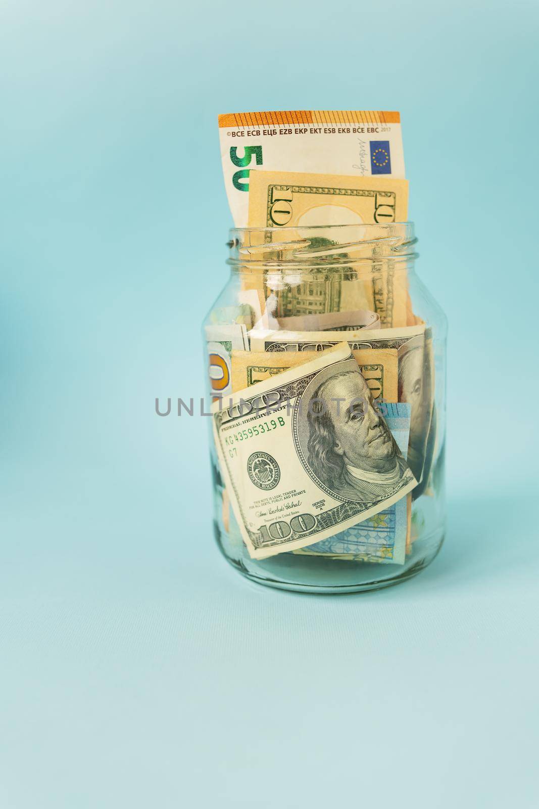 Money in international currency, including euro, dollar lies in a glass jar on a blue background. Place for an inscription