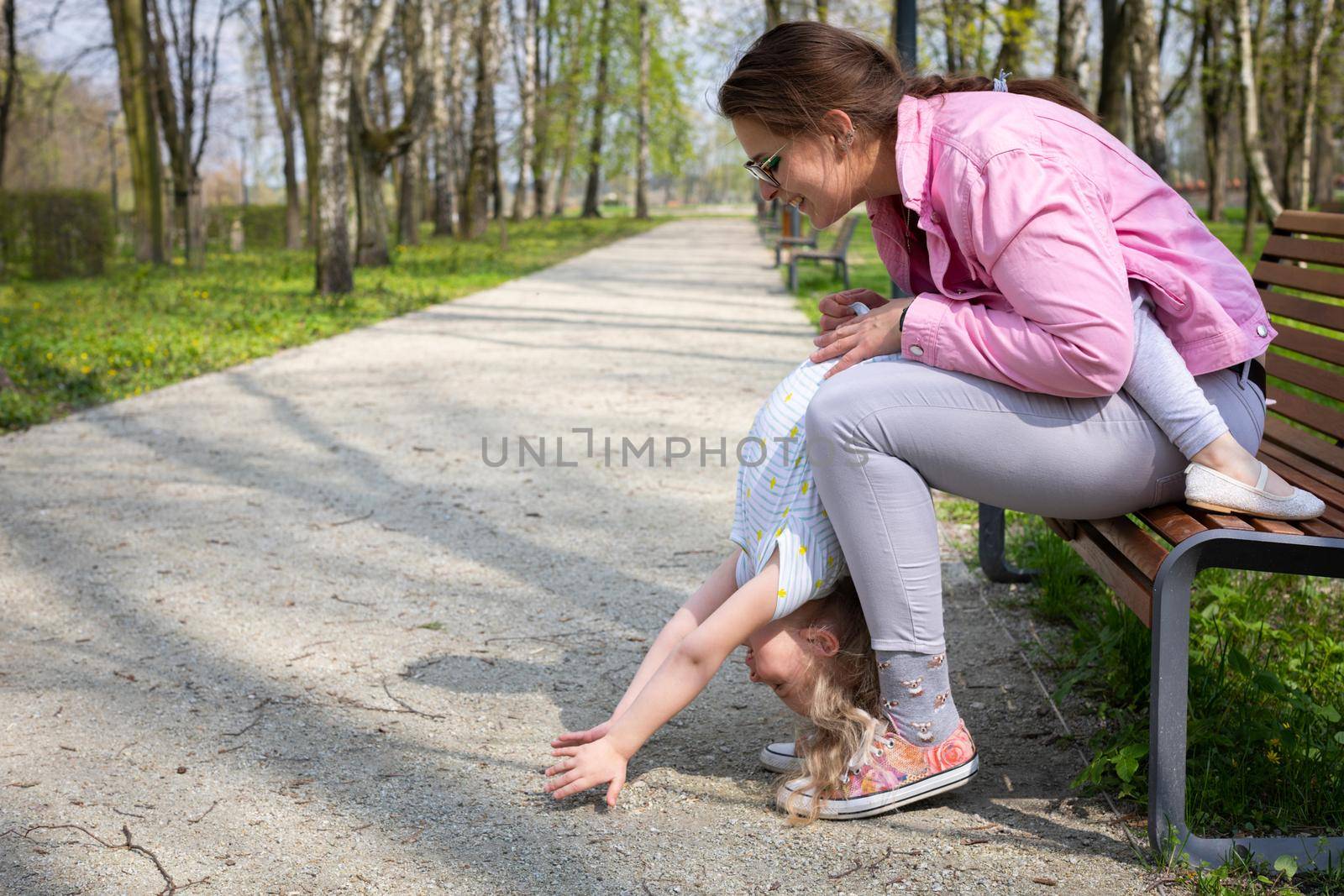 Mom and child do mini gymnastics on a bench in a city park. A movement game with abdominal muscle exercises in the child.