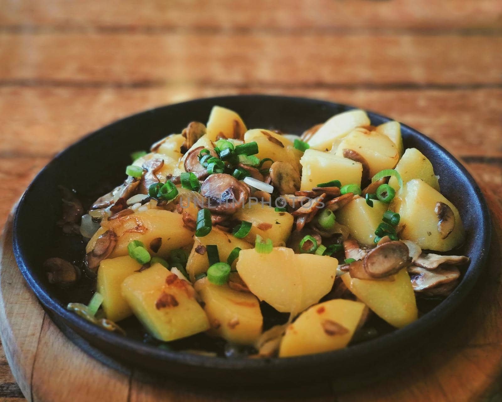 A dish of fried potatoes with mushrooms and onions in a black pan on a brown table by ProjectStockman