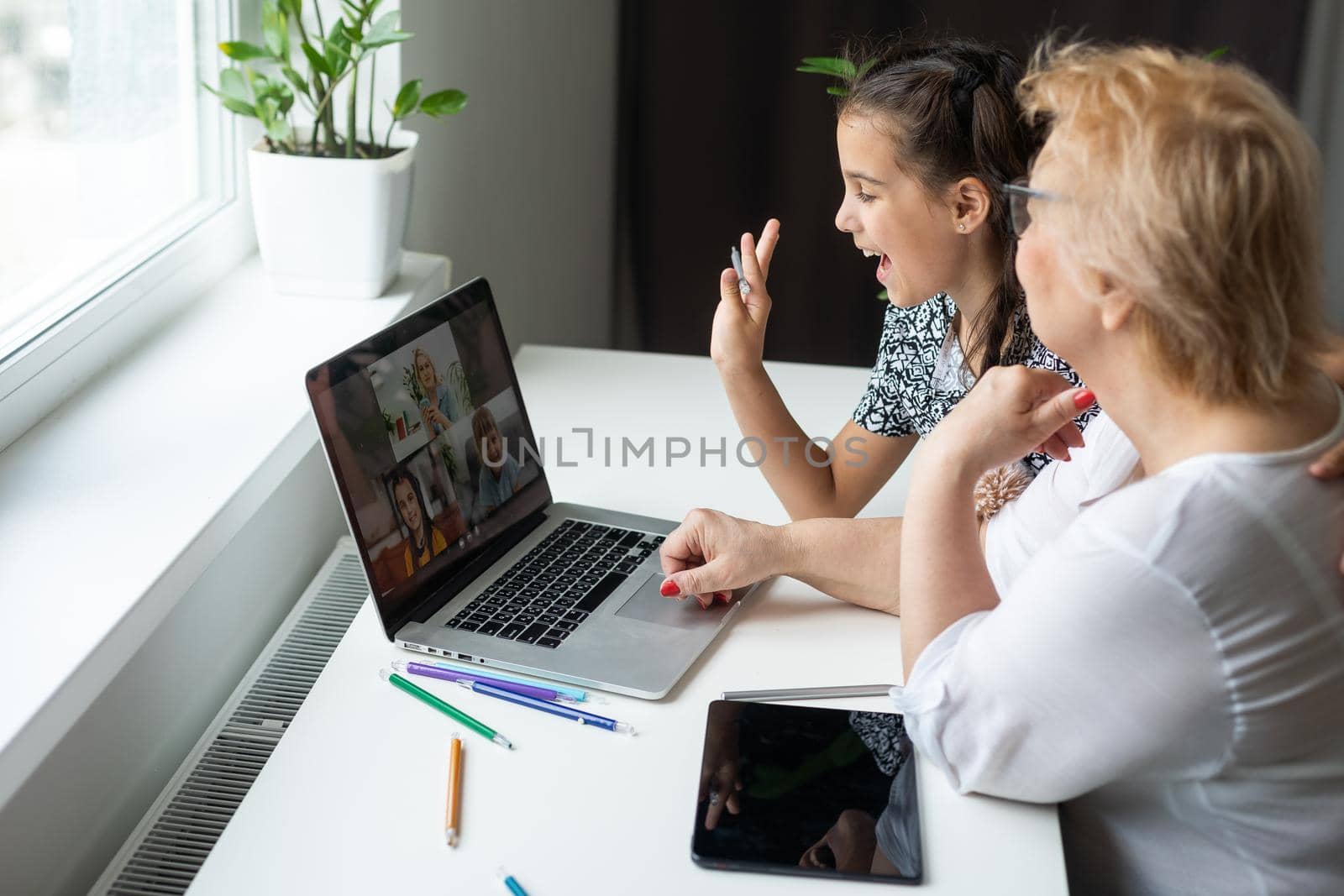 Happy grandmother and her granddaughter having video chat via laptop together at home