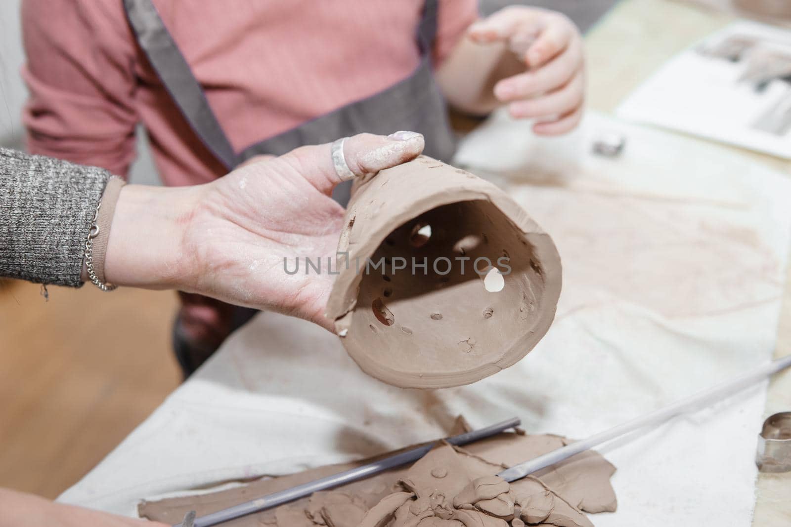 Women's hands knead clay, drawing elements of the product. Production of ceramic products at the master class on ceramics. Close-up. Making a candlestick in the form of a house. Christmas ceramic candle holder.