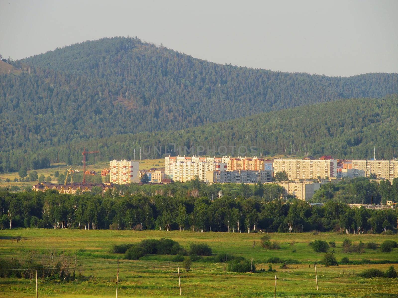 Residential houses in a lowland in the middle of mountains covered with forests illuminated by the evening sun by ProjectStockman