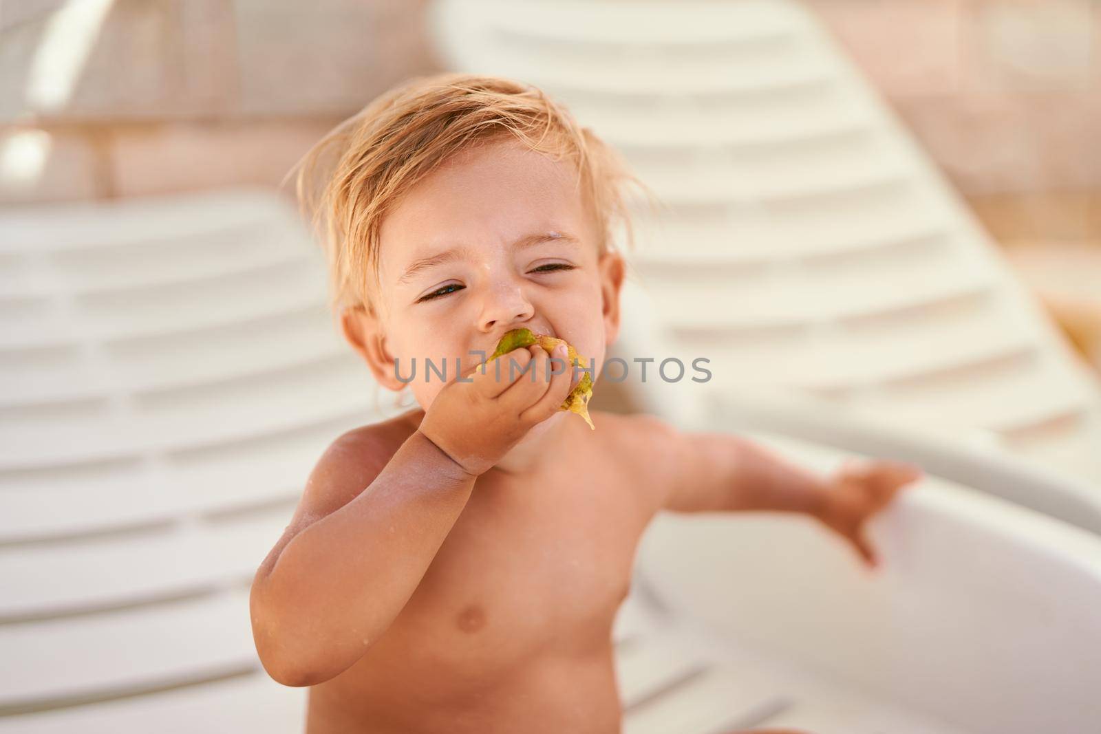 Little girl bites fruit while sitting on a sun lounger in the shade. High quality photo