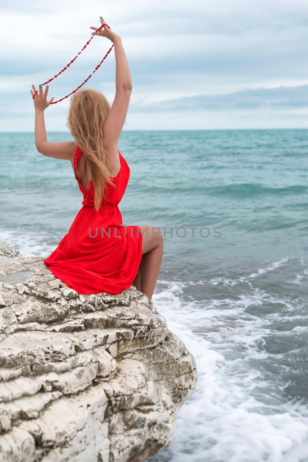 beautiful woman in a red dress on a white rock by the sea in summer