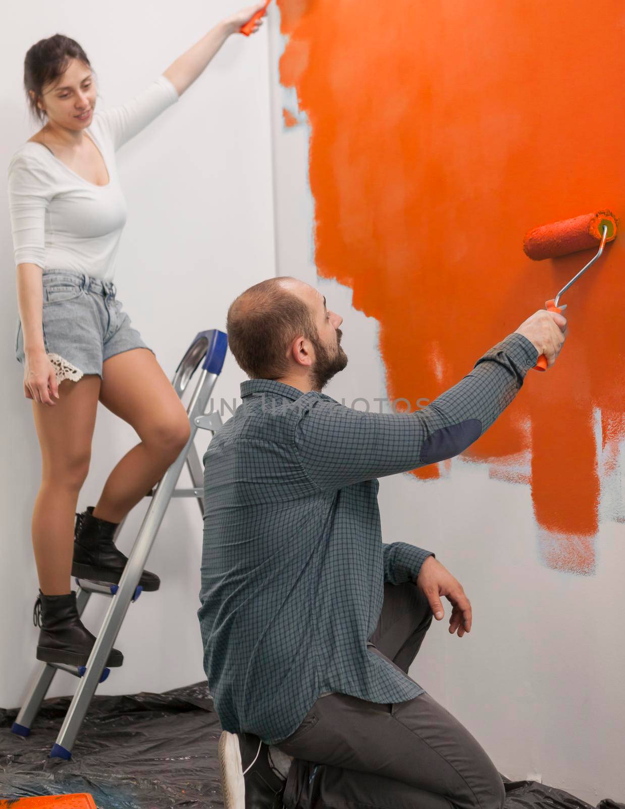 Family using orange paint to renovate apartment walls and change house design, painting with vibrant color using paintbrush, roller and tools. Diy home renovation and decoration.