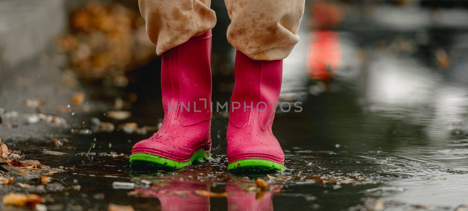 Kid wearing rubber boots standing in puddle in rainy day at autumn. Child feet in gumboots outdoors in fall season