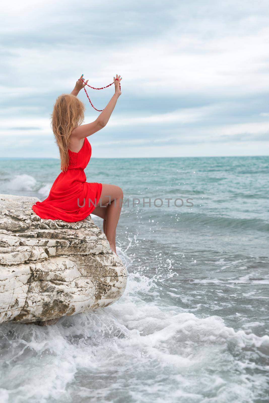 beautiful woman in a red dress on a white rock by the sea in summer