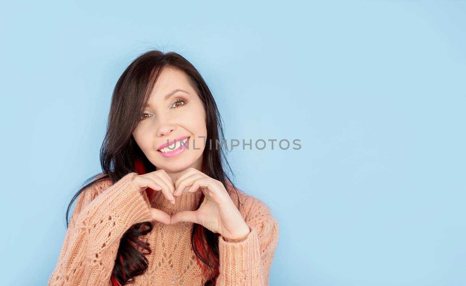 Smiling young american girl in casual coral knitted clothes showing shape heart with hands isolated on pastel blue background. People lifestyle concept. Mock up copy space. Heart-shape sign. by JuliaDorian