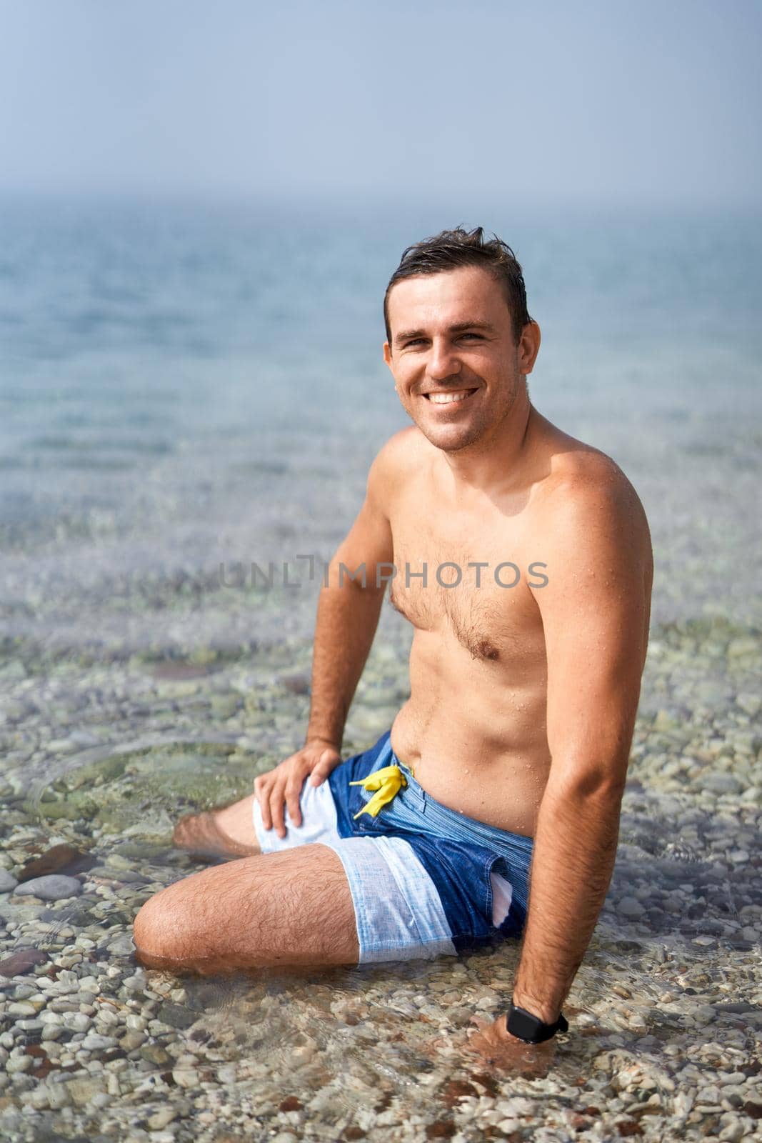 Young smiling man sitting in the water near the shore. High quality photo