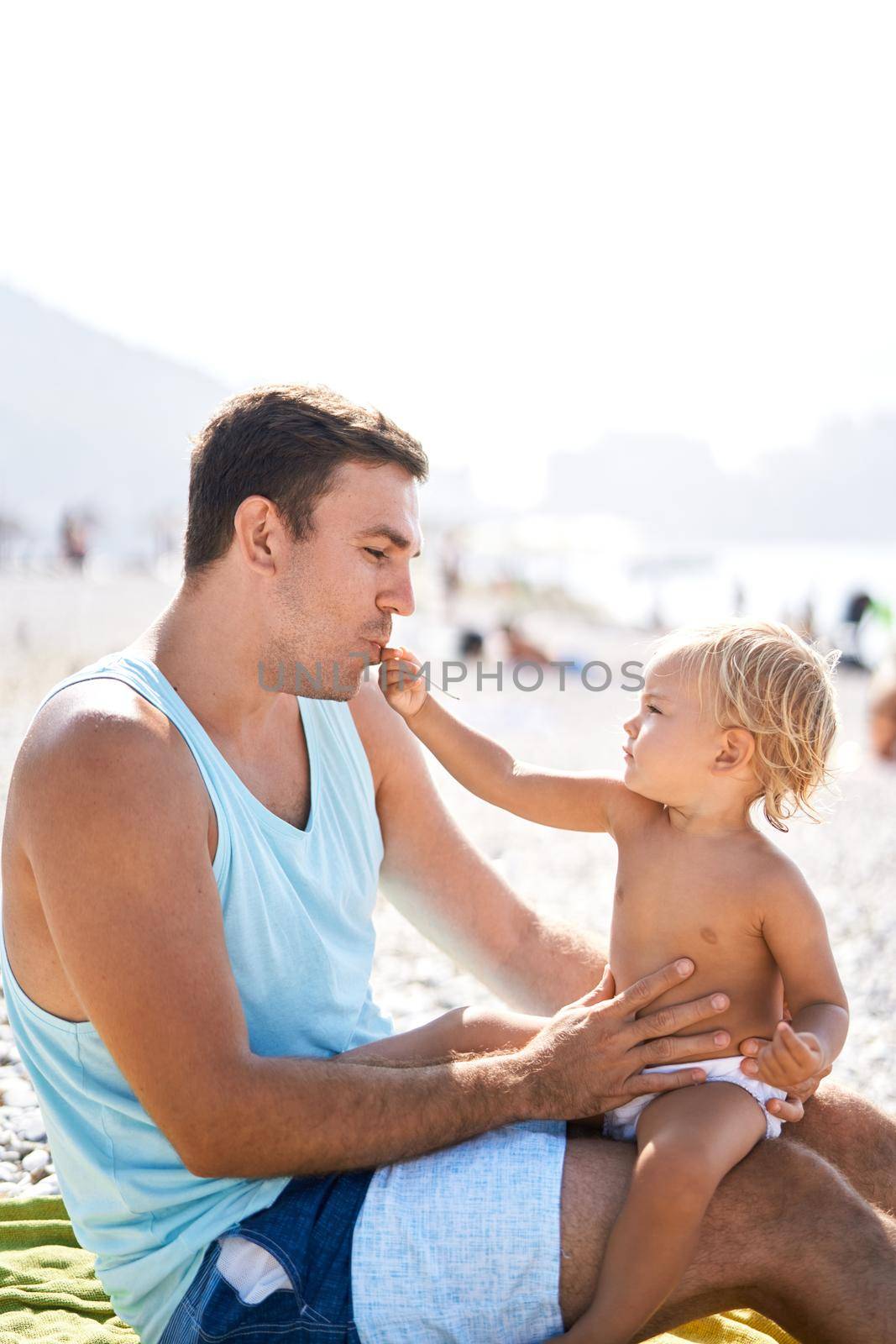 Little daughter spoon-feeds her dad while sitting on the beach. High quality photo