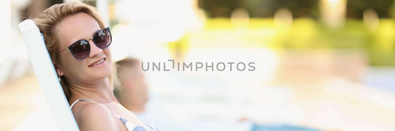 Portrait of happy young blonde woman lay on sunbed in pretty summer outfit. Beautiful relaxed female in sunglasses enjoy weather. Summer, leisure concept