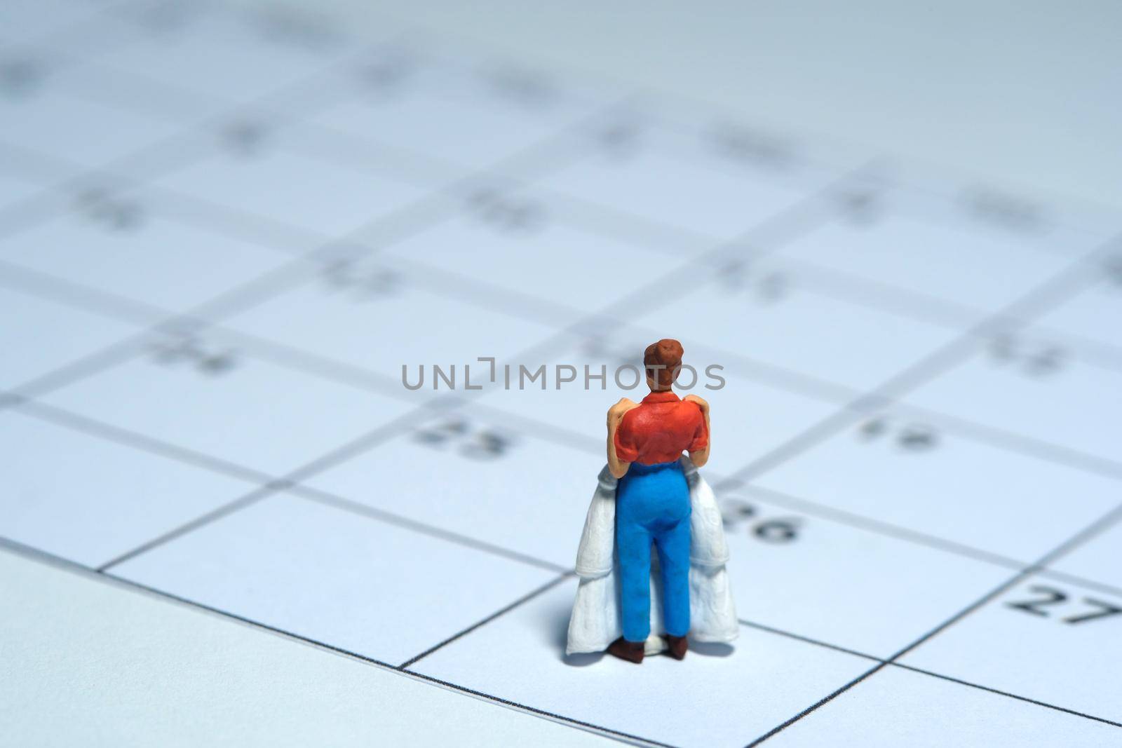 Woman miniature people stand above calendar while holding wedding dress, fitting day concept. Image photo by Macrostud