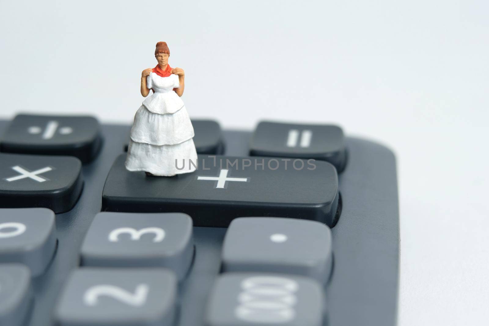 Wedding dress budget for bride, miniature people illustration concept. Woman standing above calculator. Image photo by Macrostud