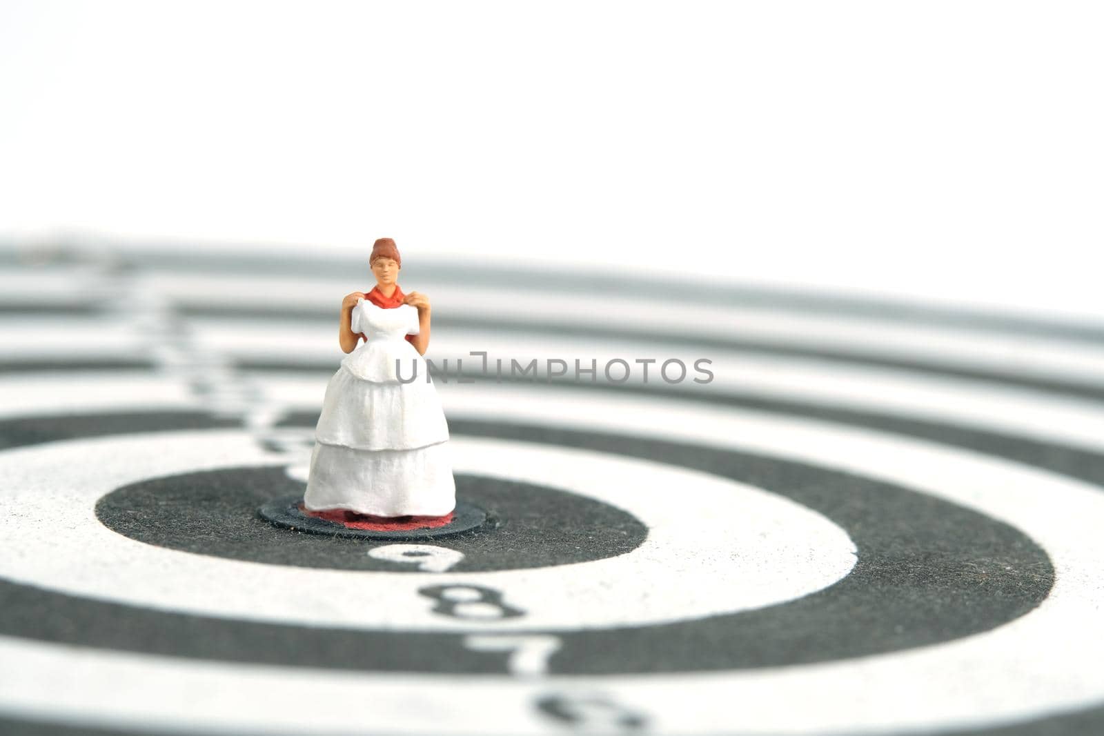Wedding married target goal conceptual miniature people toy photography. Women trying wedding dress standing on dartboard. Image photo by Macrostud