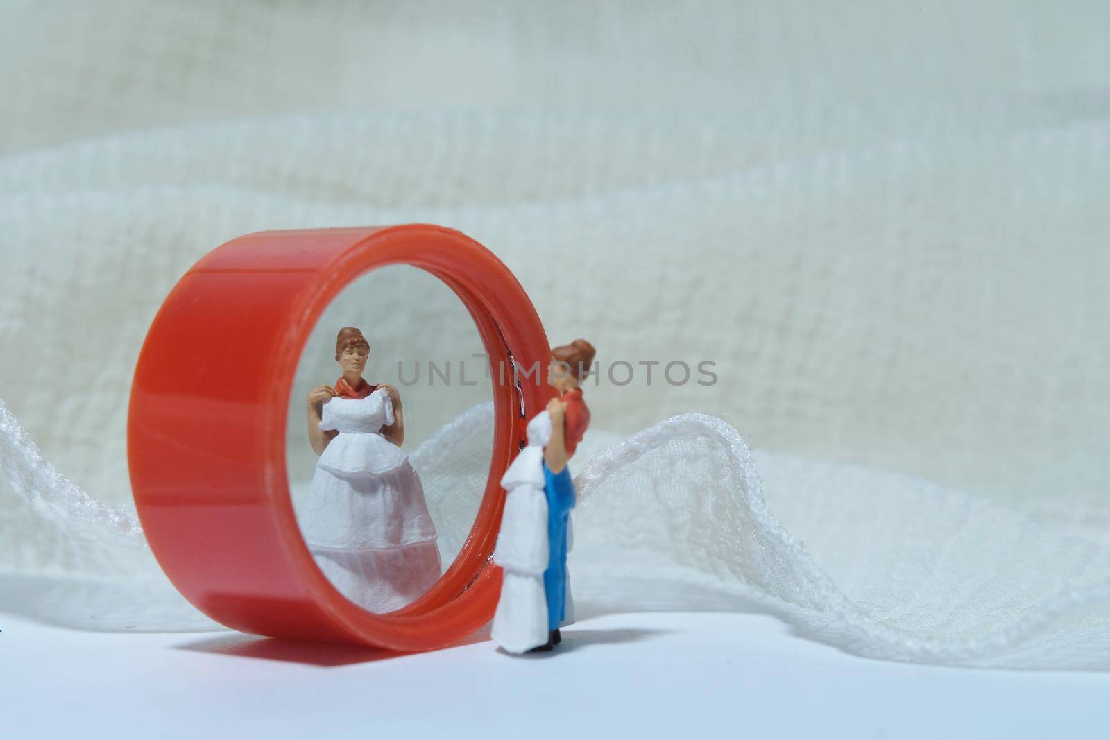 Women miniature people stand in front of mirror trying wedding dress. Image photo