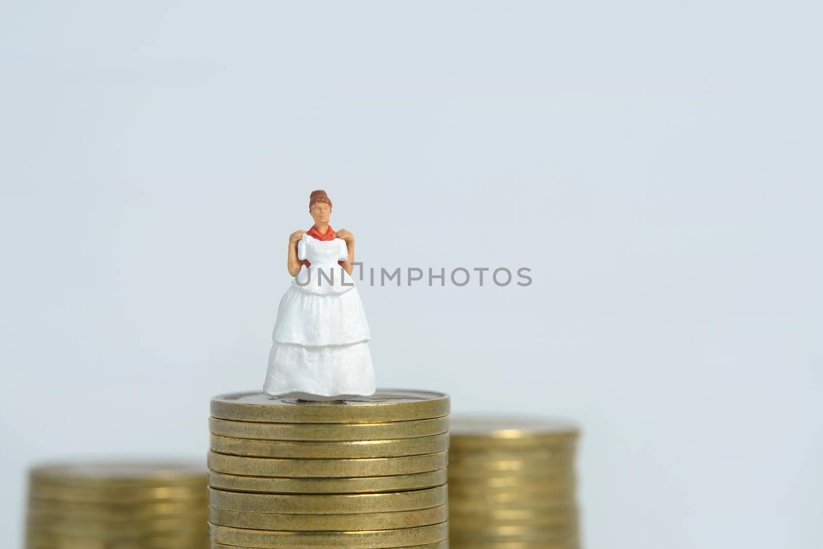 Wedding dress budget for bride, miniature people illustration concept. Woman standing above coin money stack. Image photo by Macrostud