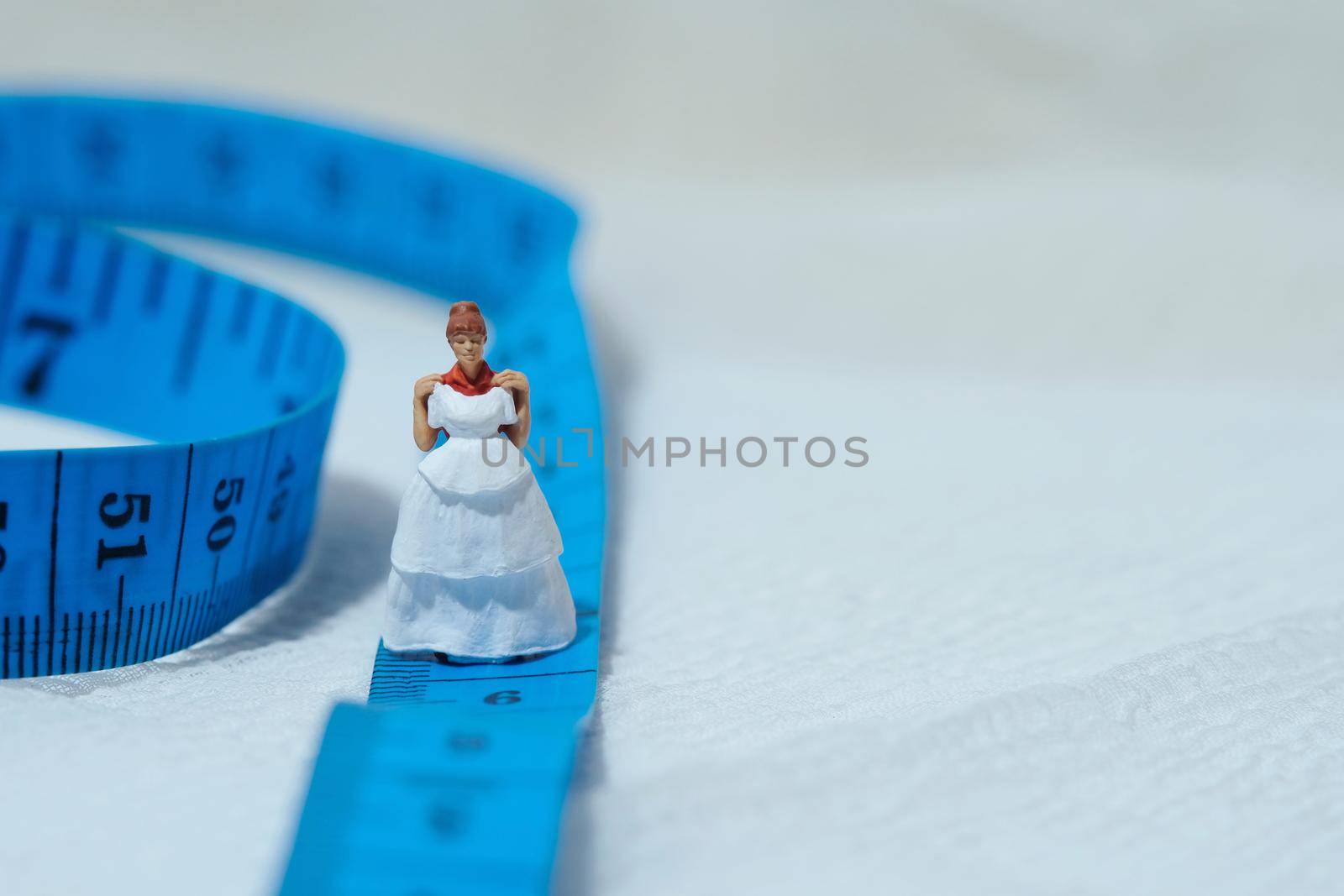 Women miniature people standing above measuring tape to fix her wedding dress. Image photo by Macrostud