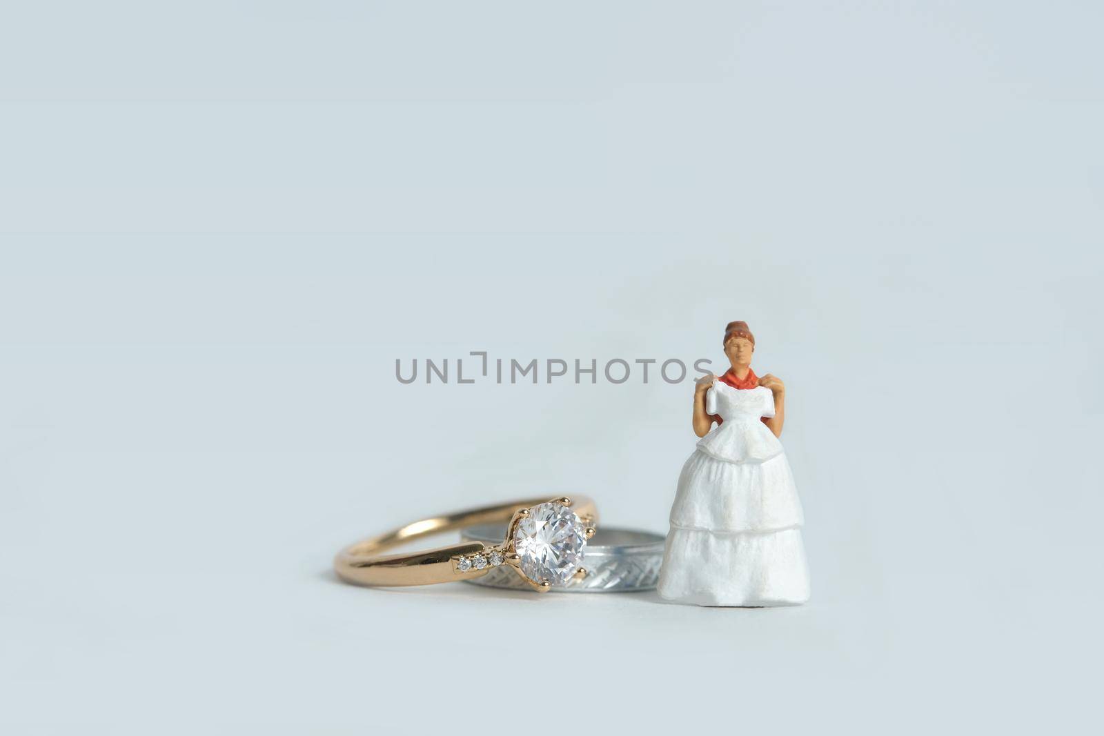 Women miniature people fitting wedding dress standing in front of couple ring, isolated white background. Image photo